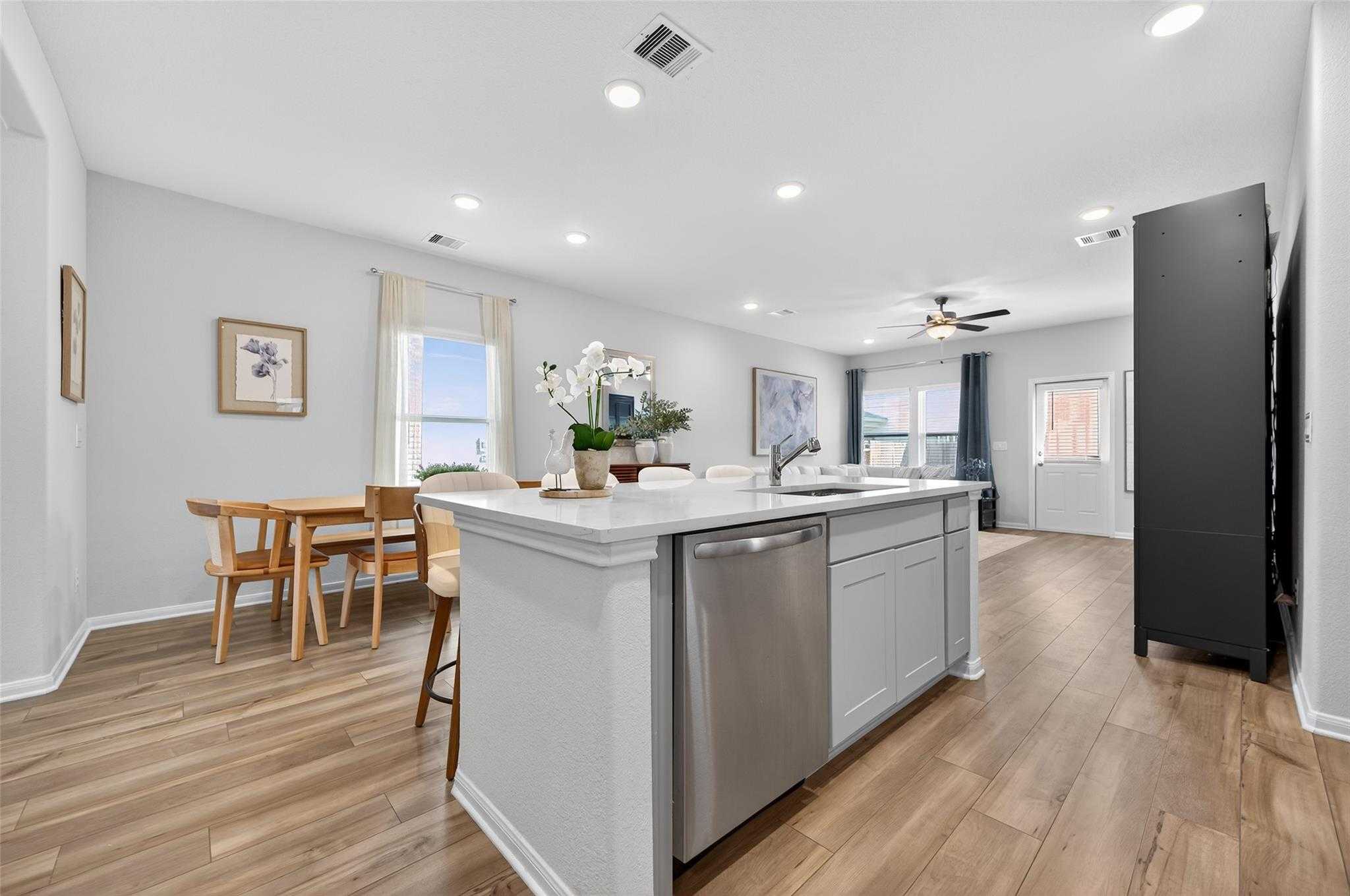 Bright open-concept kitchen with white island, stainless dishwasher, orchids, and dining table in Davidson Homes The Brazos E, Magnolia Texas