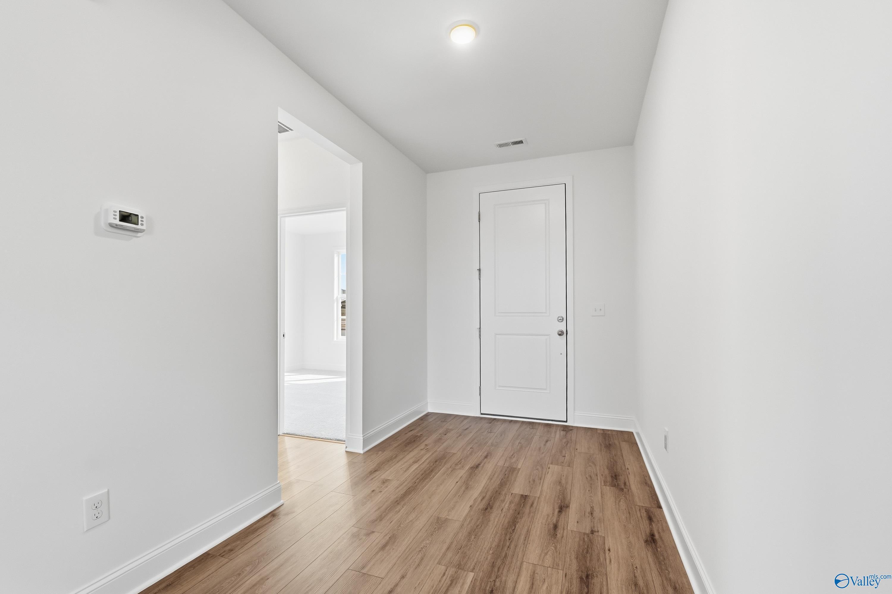 Bright hallway with luxury vinyl plank flooring, open bathroom doorway, and white paneled door in Davidson Homes Montgomery C, Harvest, Alabama