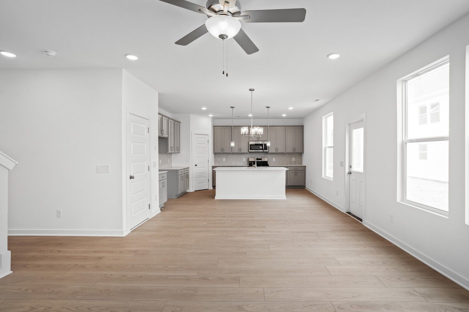Open-concept kitchen and great room with white island, stainless appliances, hardwood floors, and staircase in Davidson Homes The Logan B, Calista Farms