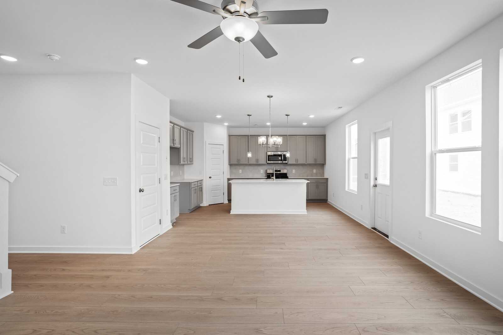 Open-concept kitchen and great room with white island, stainless appliances, hardwood floors, and staircase in Davidson Homes The Logan B, Calista Farms