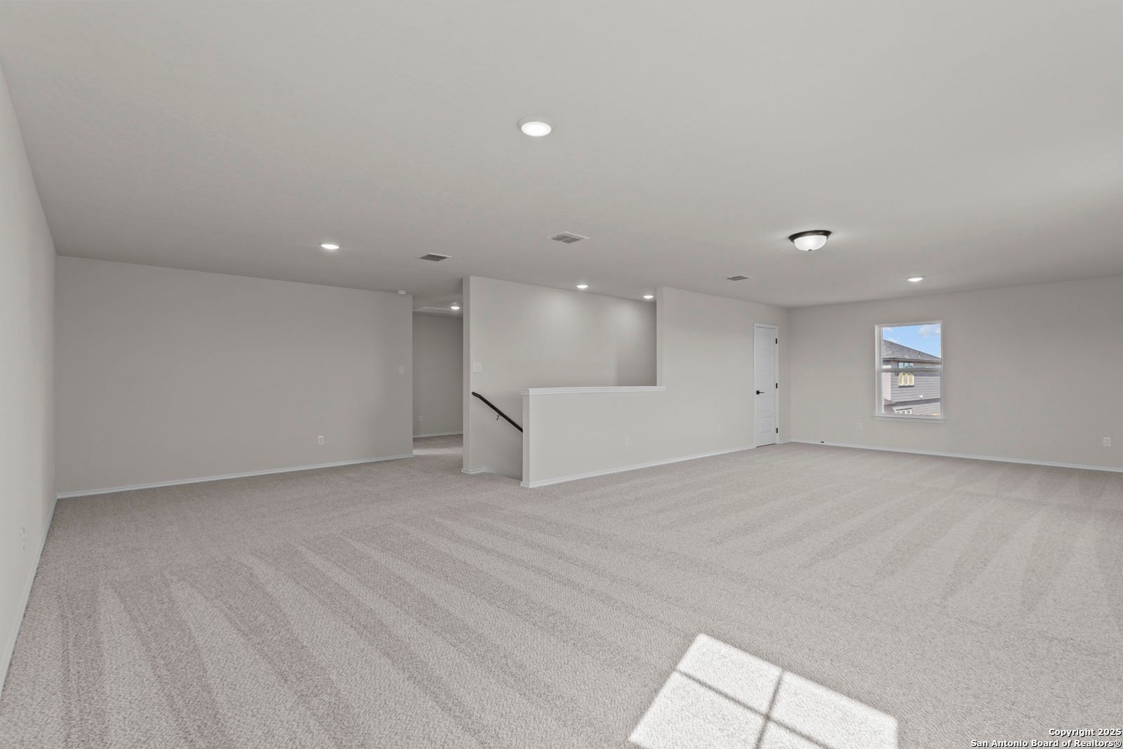 Spacious upstairs loft with gray carpet, recessed lights, half-wall staircase, and window in Davidson Homes The Douglas C, Seguin, Texas