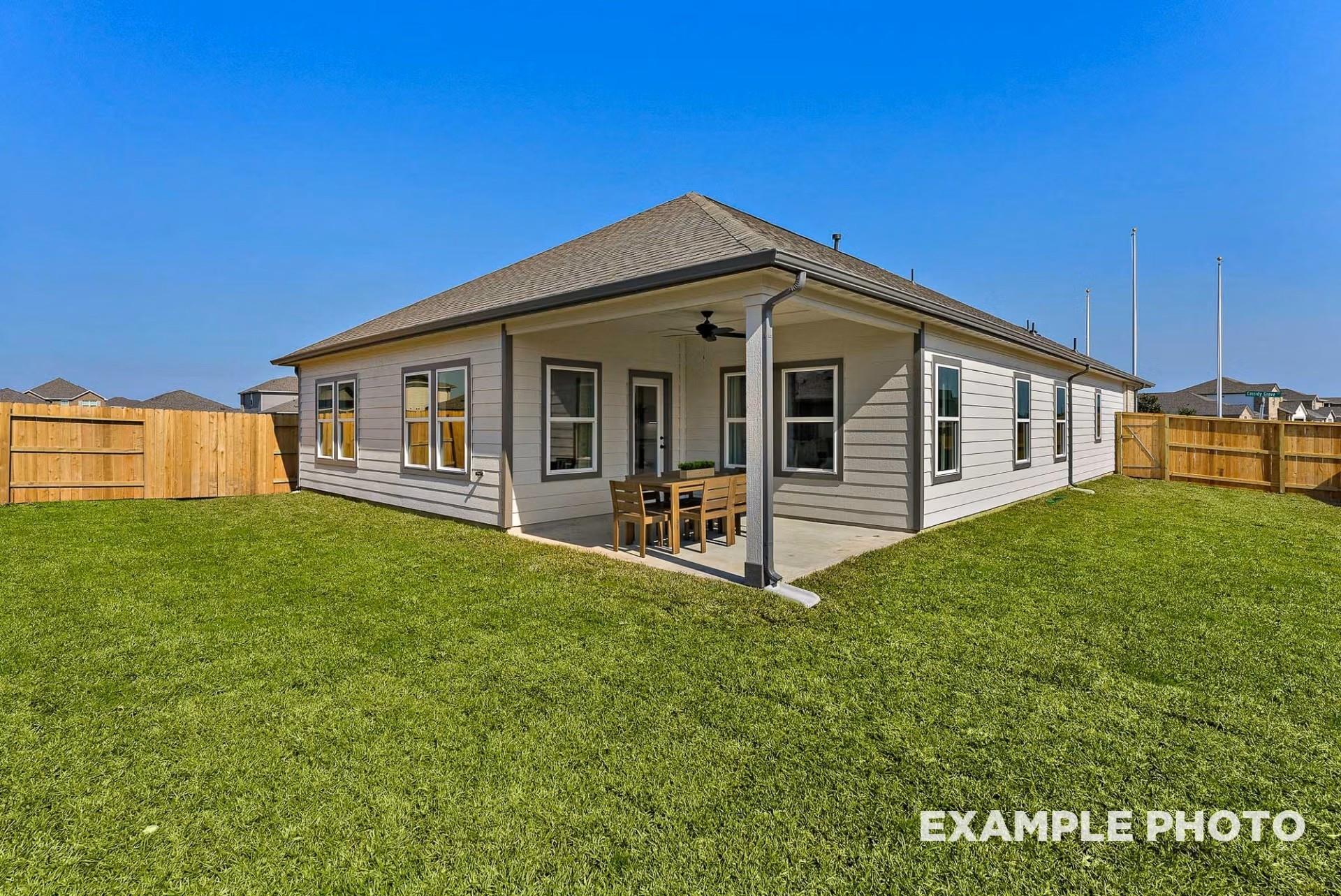Covered patio with ceiling fan and wooden dining set on lush green lawn of Davidson Homes The Everett C in River Ranch Meadows, Dayton, Texas
