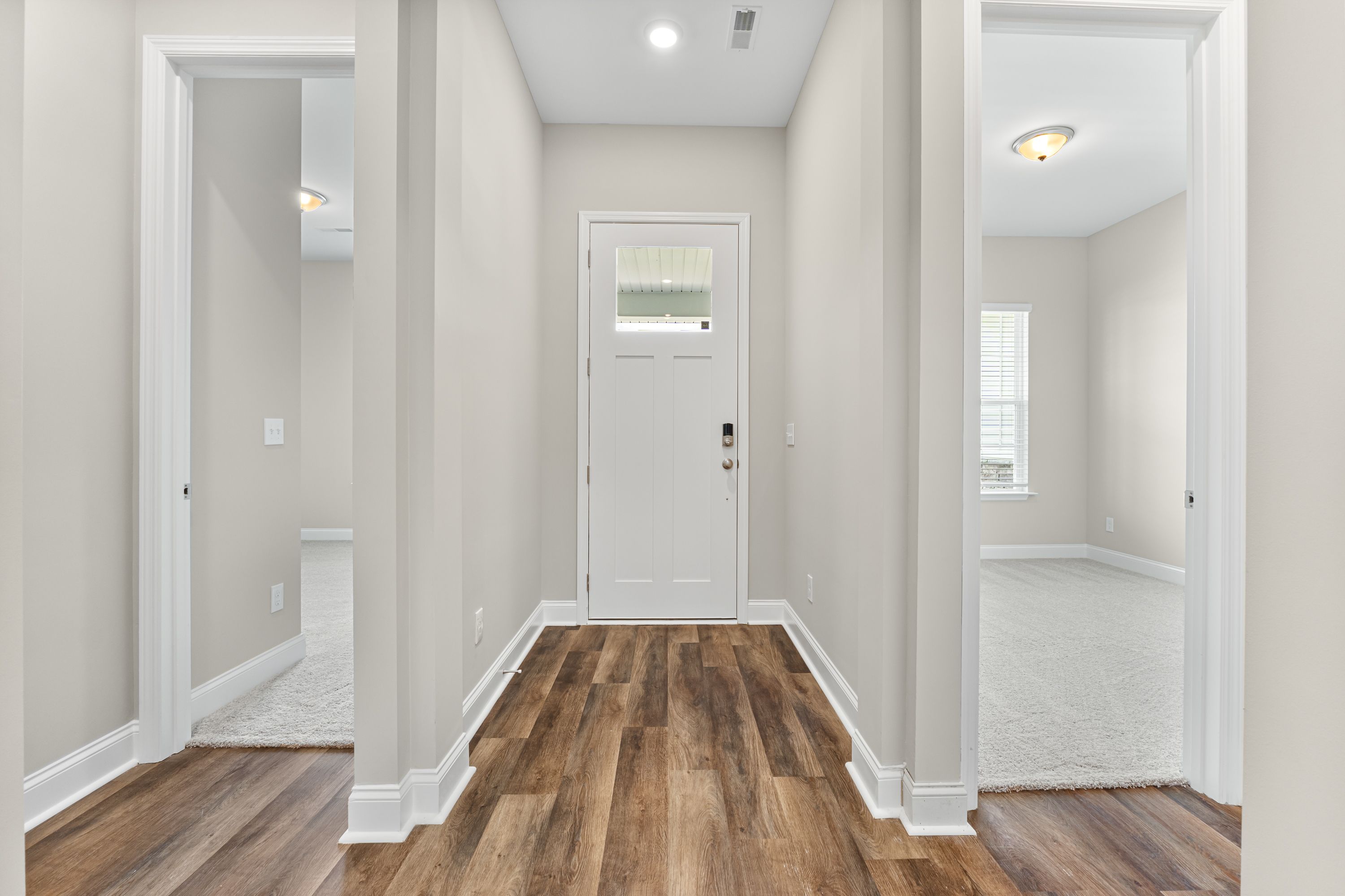 Spacious entry foyer of The Arcadia E home with white front door, hardwood plank floors, light gray walls, and adjacent carpeted rooms