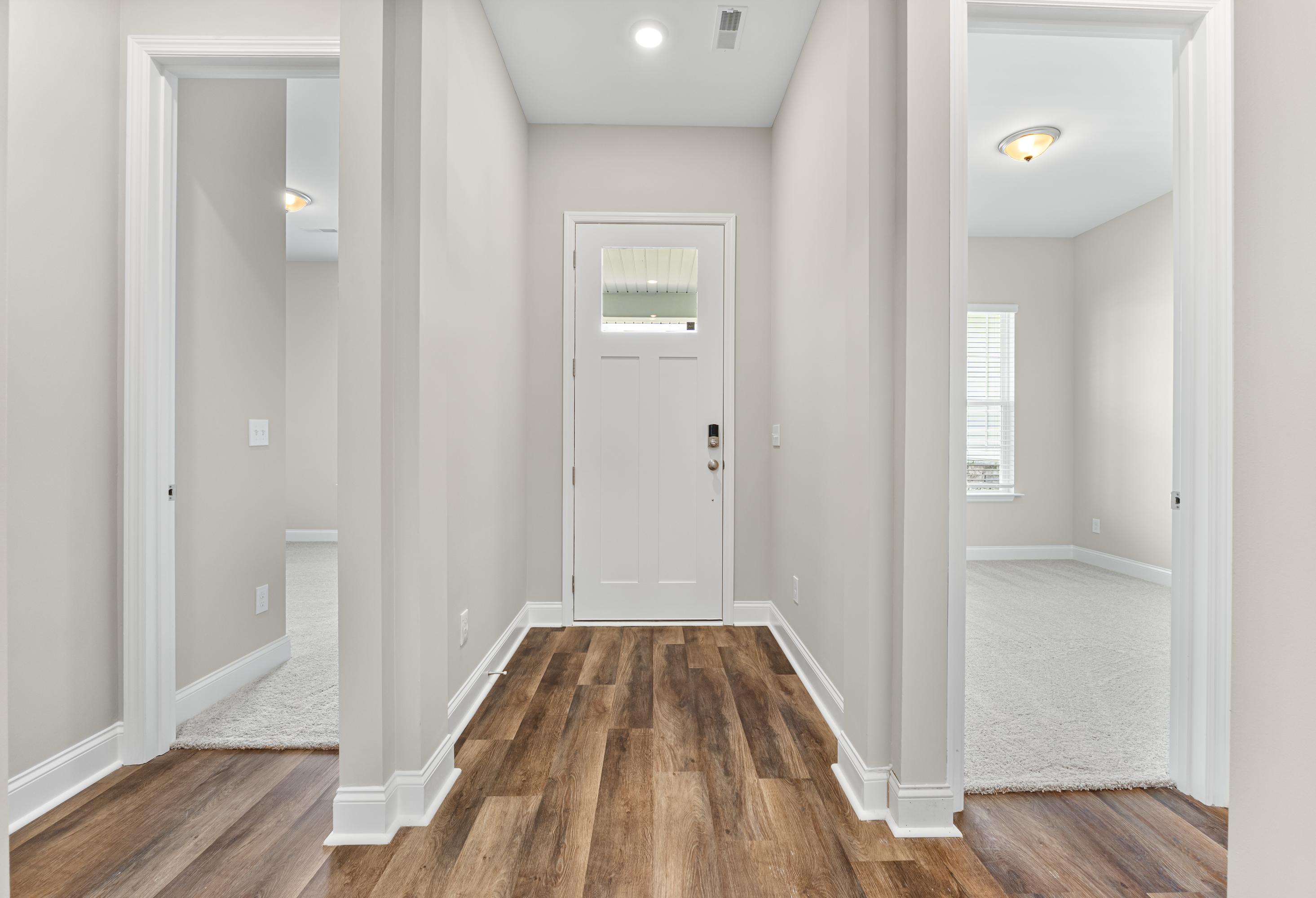 Spacious entry foyer of The Arcadia E home with white front door, hardwood plank floors, light gray walls, and adjacent carpeted rooms