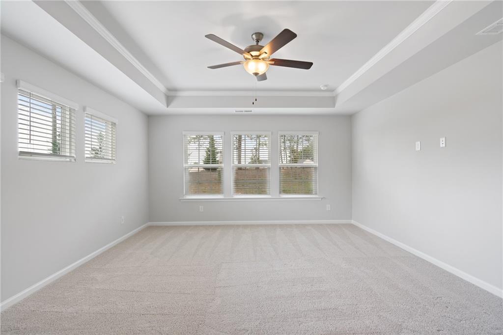 Spacious empty bedroom with tray ceiling, lighted fan, and triple windows in Davidson Homes The Hickory A, Winder, GA