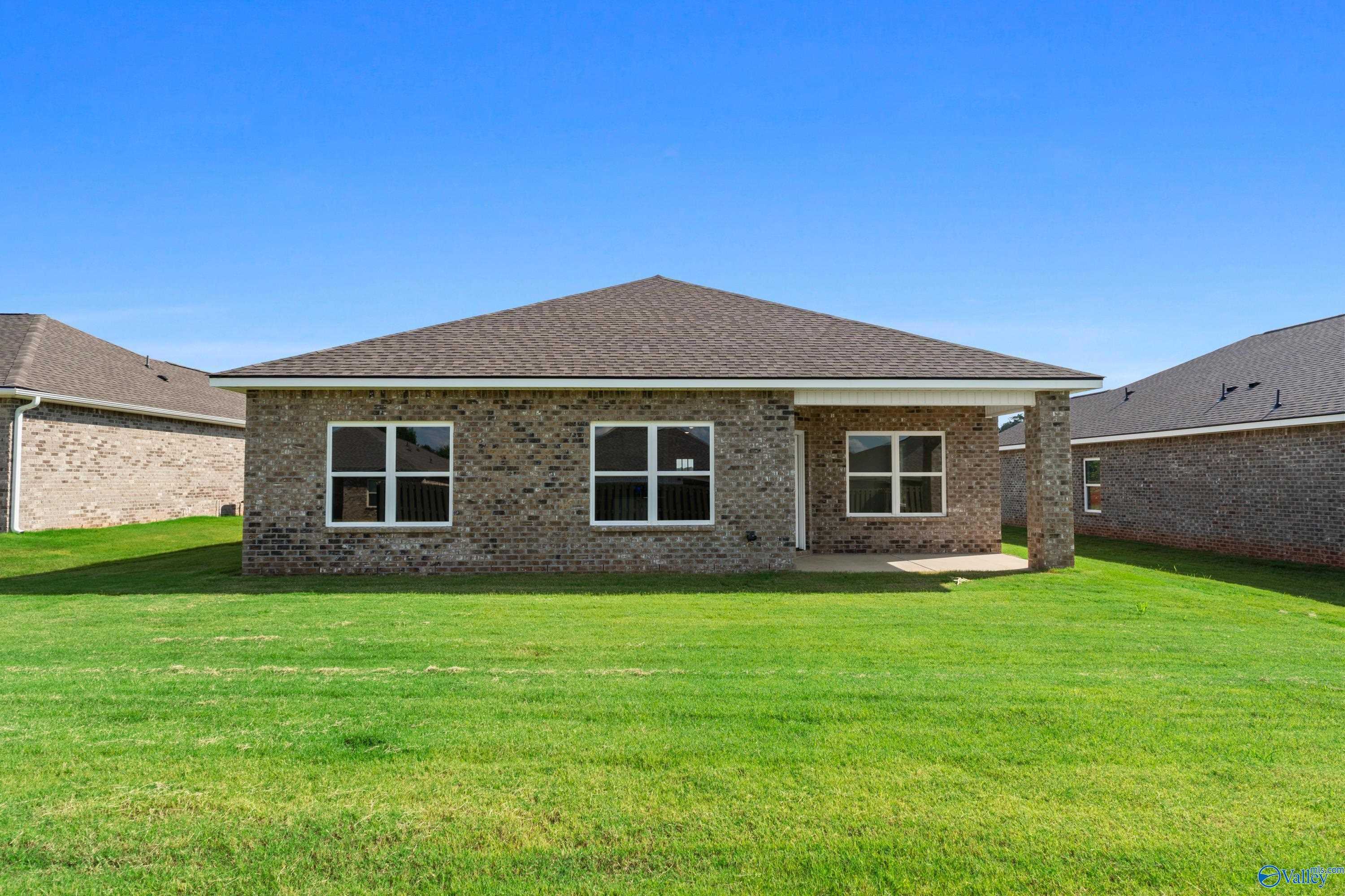Single-story brick home with covered back patio, large windows, and lush green yard in Clearview, Hazel Green, Alabama by Davidson Homes