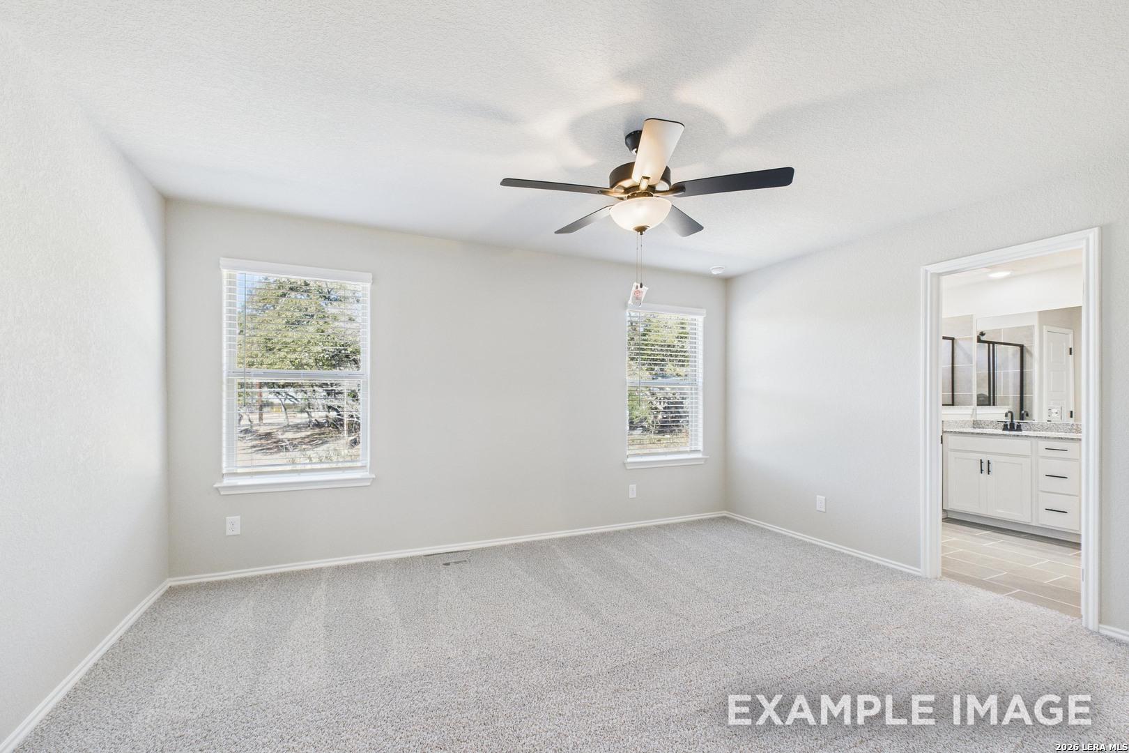 Bright bedroom with neutral carpet, ceiling fan, and en-suite bathroom in The Charlotte B floor plan, Cedar Heights.