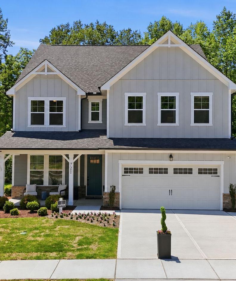 Two-story gray farmhouse style home with covered front porch and American flag at Wendell Ridge by Davidson Homes in Wendell, NC