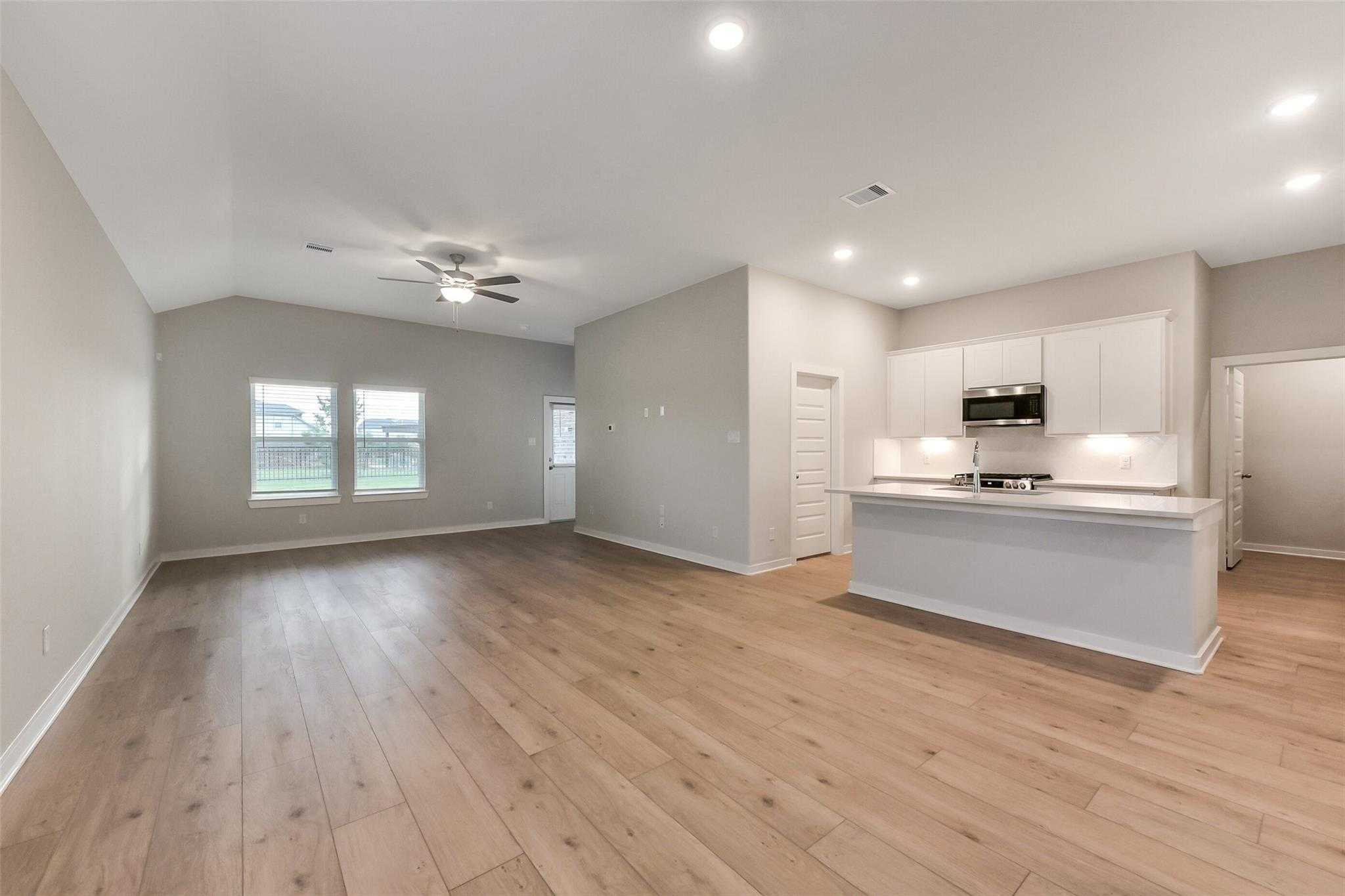 Open-concept living-kitchen with wood floors, white cabinets, island sink and ceiling fan in Davidson Homes The Laguna B, Katy, Texas