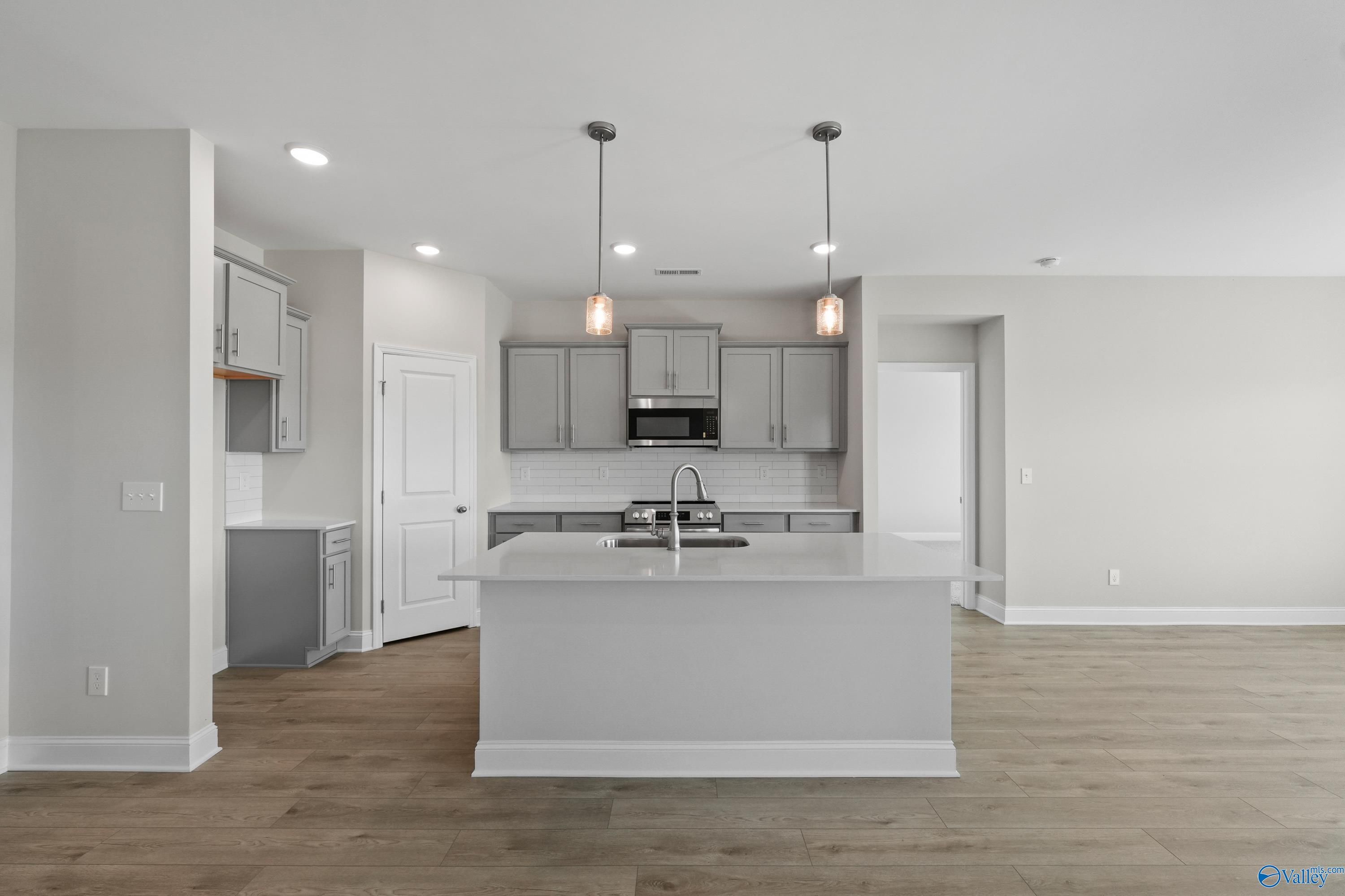 Modern open-concept kitchen with white island sink, stainless appliances, and pendant lights in The Everett 4-bedroom home, Hazel Green, Alabama