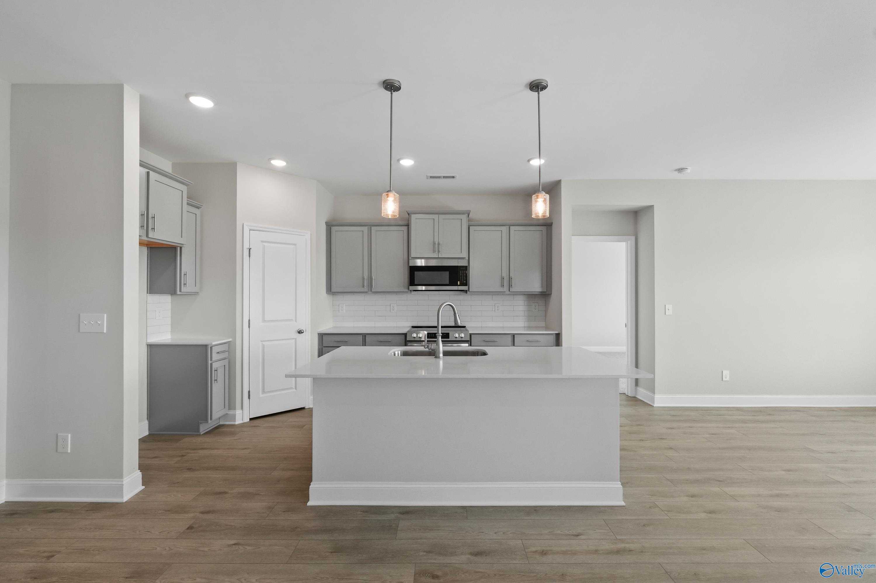 Modern open-concept kitchen with white island sink, stainless appliances, and pendant lights in The Everett 4-bedroom home, Hazel Green, Alabama
