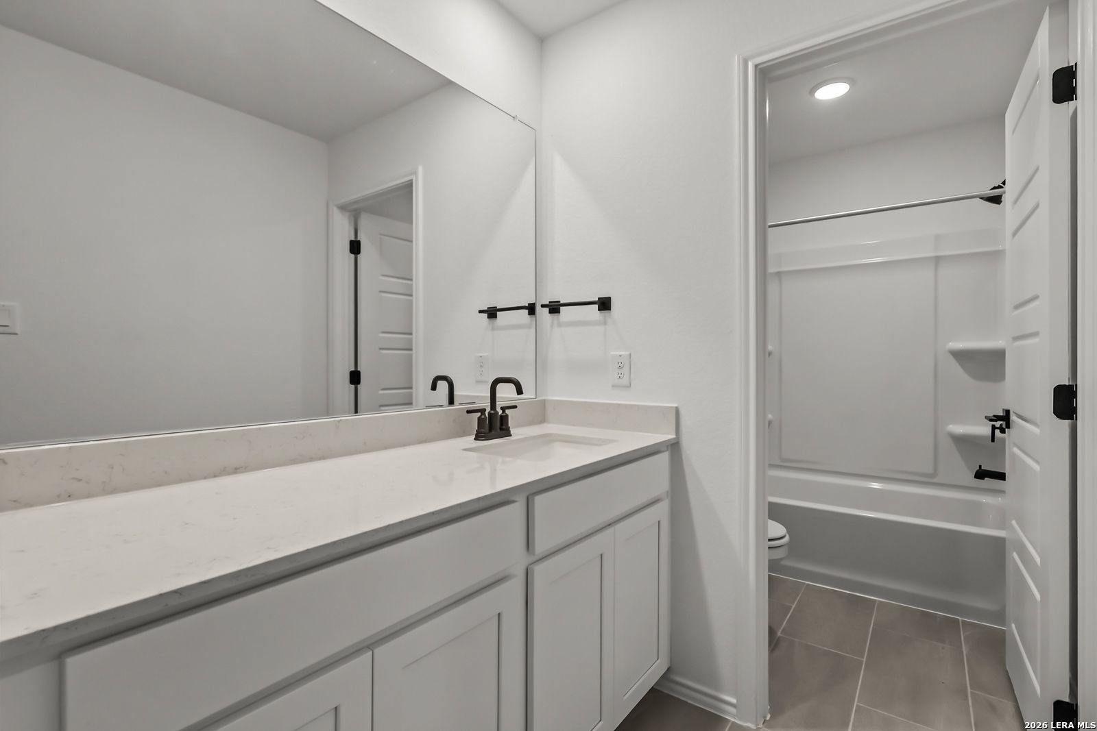 Modern bathroom with white vanity, quartz countertop, and tub-shower combo in The Florence B home, Meadows at Oak Creek.