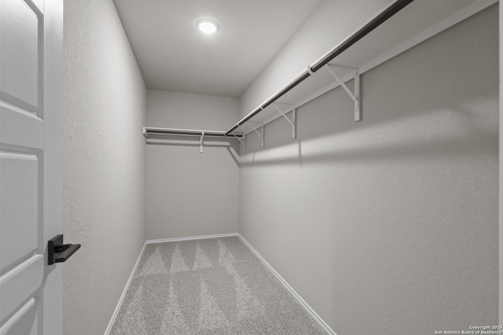 Spacious walk-in closet with white walls, carpeted floor, and built-in hanging rods in The Murray J by Davidson Homes, San Antonio