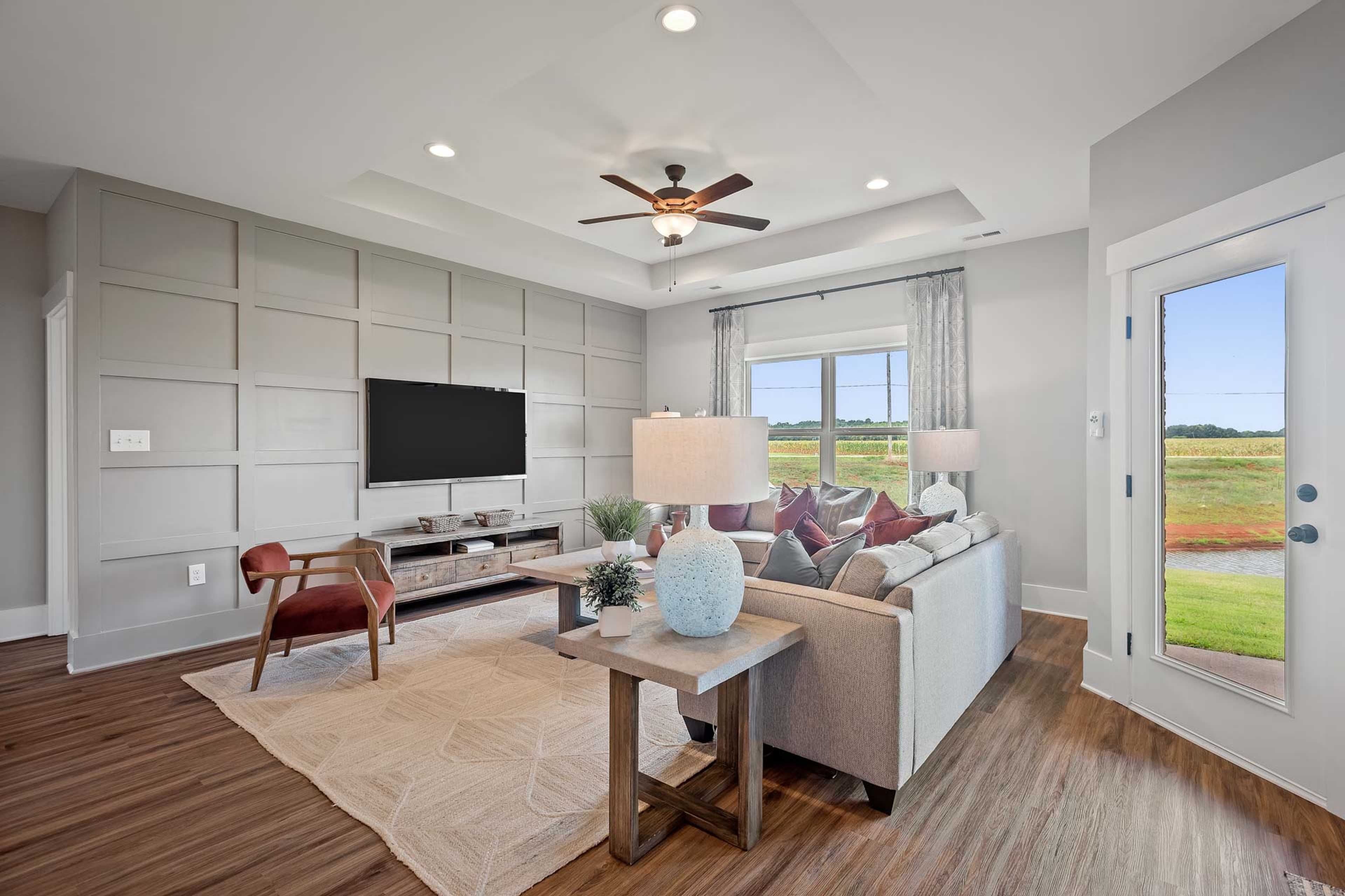 Spacious living room at Heritage Lakes in New Market, Alabama with gray shiplap walls, hardwood floors, gray sectional sofa, and lake views