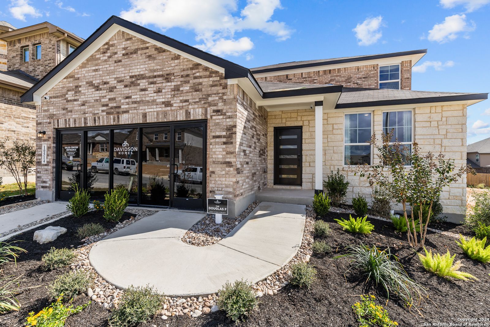 Modern two-story brick home with large front windows, black door, and curved stone pathway in Bricewood, San Antonio, Texas