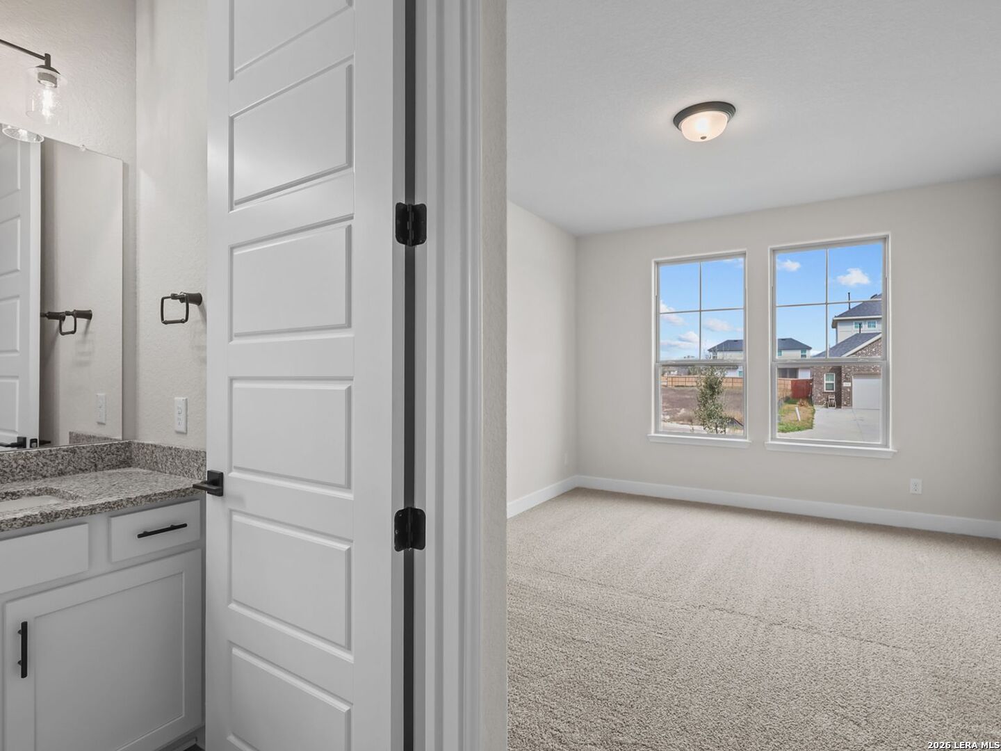 Bright bedroom with carpet and attached bathroom featuring granite vanity in The Belmont H floor plan, Castroville, TX.