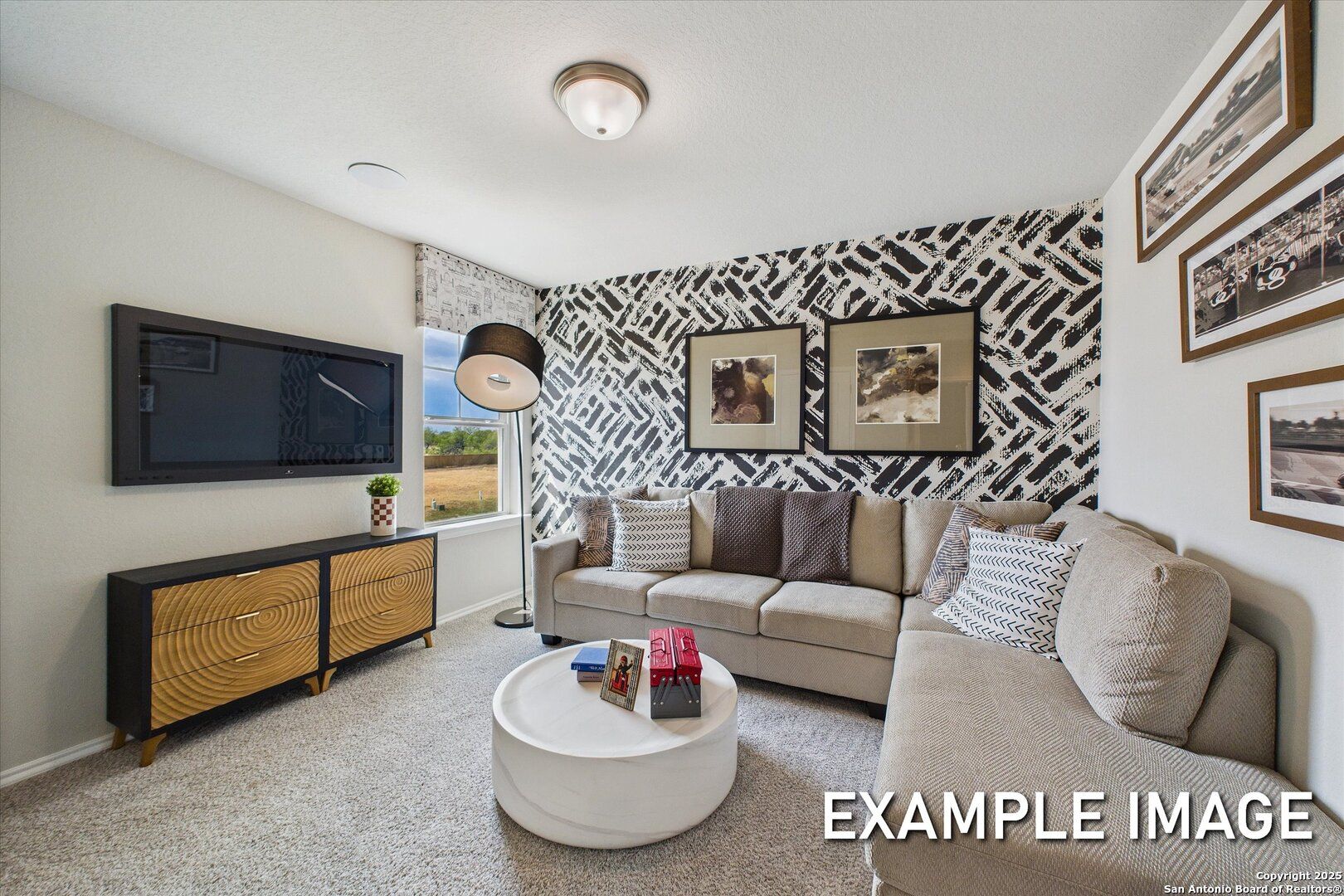 Cozy modern living room with beige sectional sofa, wall-mounted TV, abstract art, and patterned wall in Davidson Homes The Sabine C, San Antonio