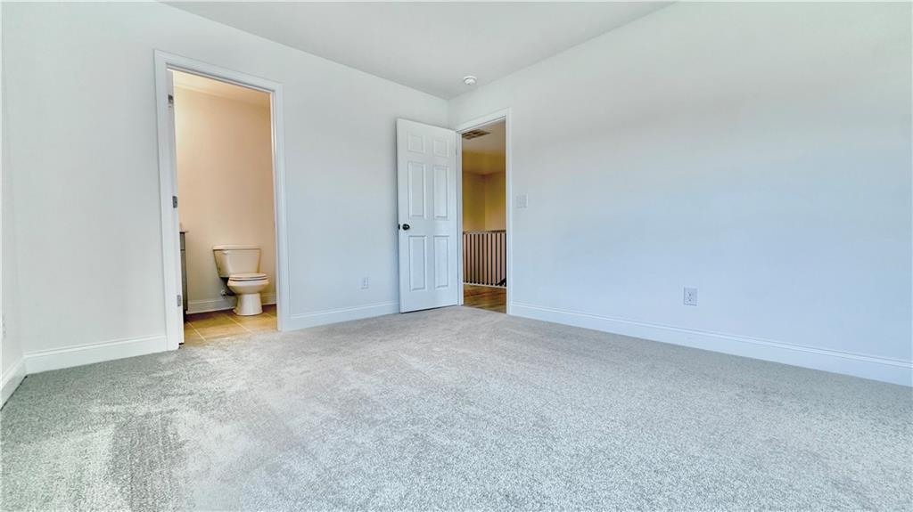 Spacious carpeted bedroom with an en-suite bathroom in The Hickory C floor plan at Wehunt Meadows, Hoschton, Georgia.
