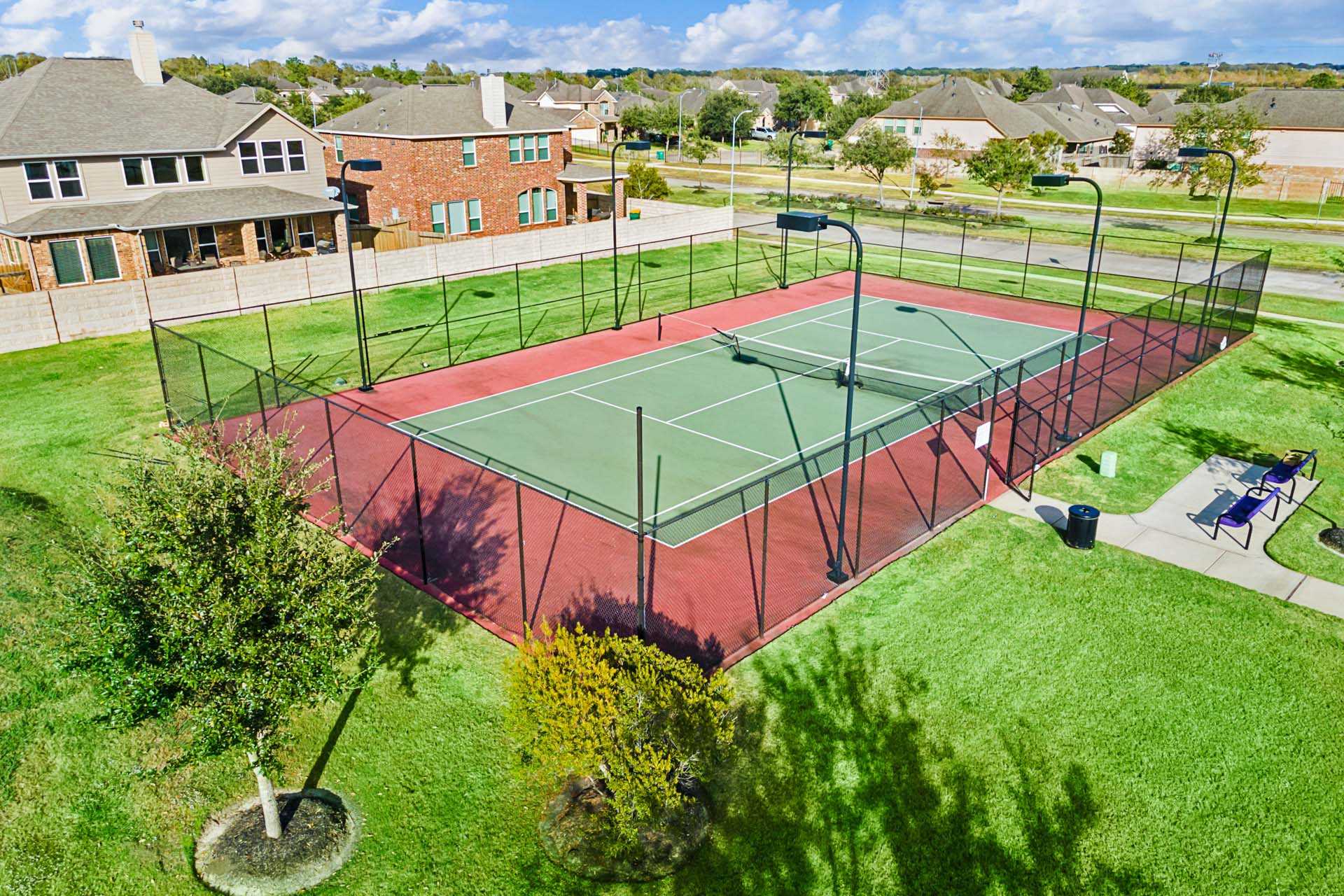 Aerial view of fenced red tennis courts at Sierra Vista in Rosharon, Texas with benches and neighborhood homes