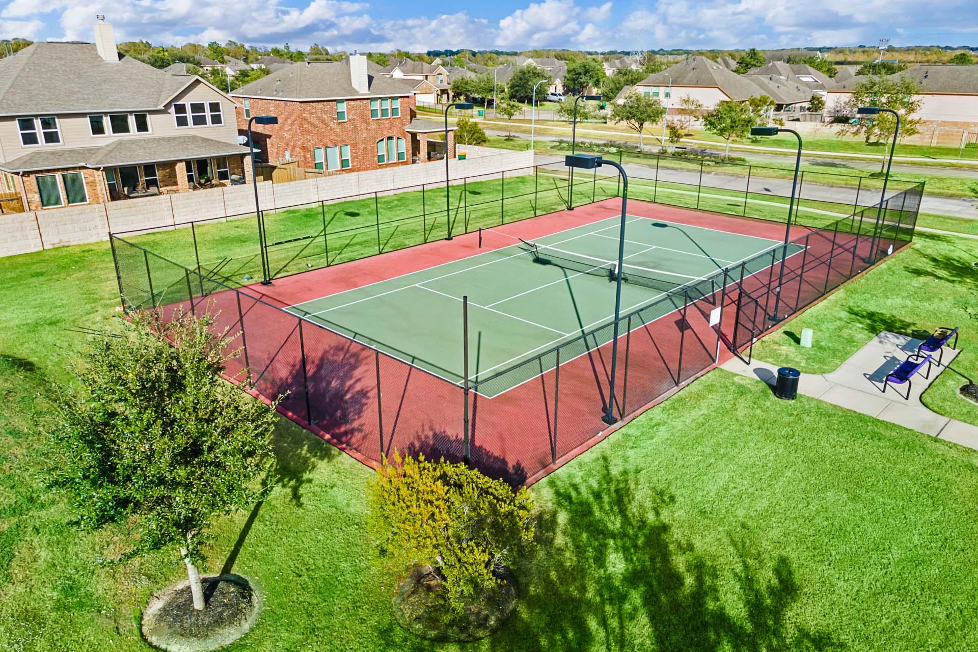 Aerial view of fenced red tennis courts at Sierra Vista in Rosharon, Texas with benches and neighborhood homes