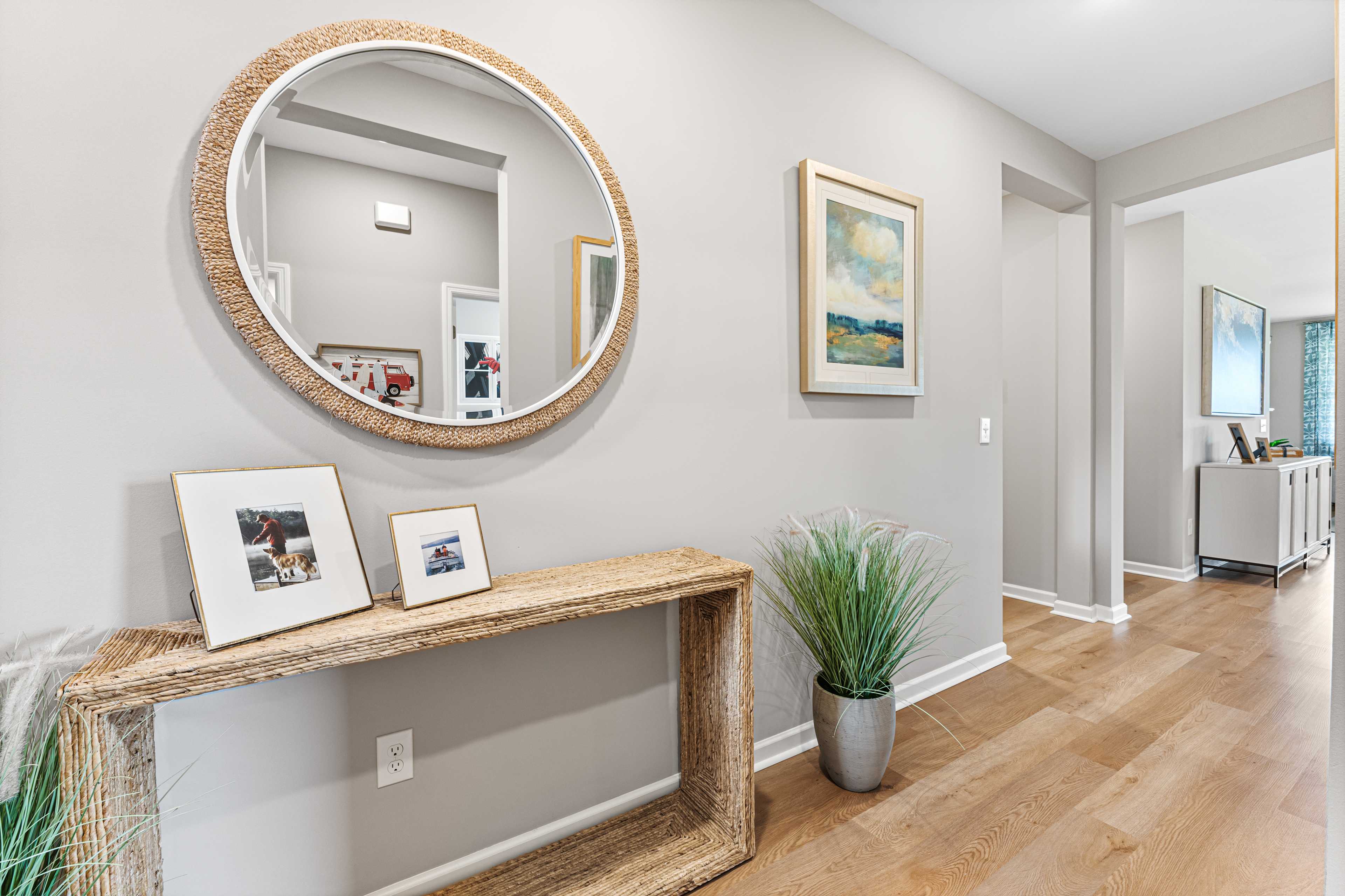 Elegant entryway at Forest Glen in Hazel Green AL featuring rattan mirror, woven console table, potted plant, and hardwood floors