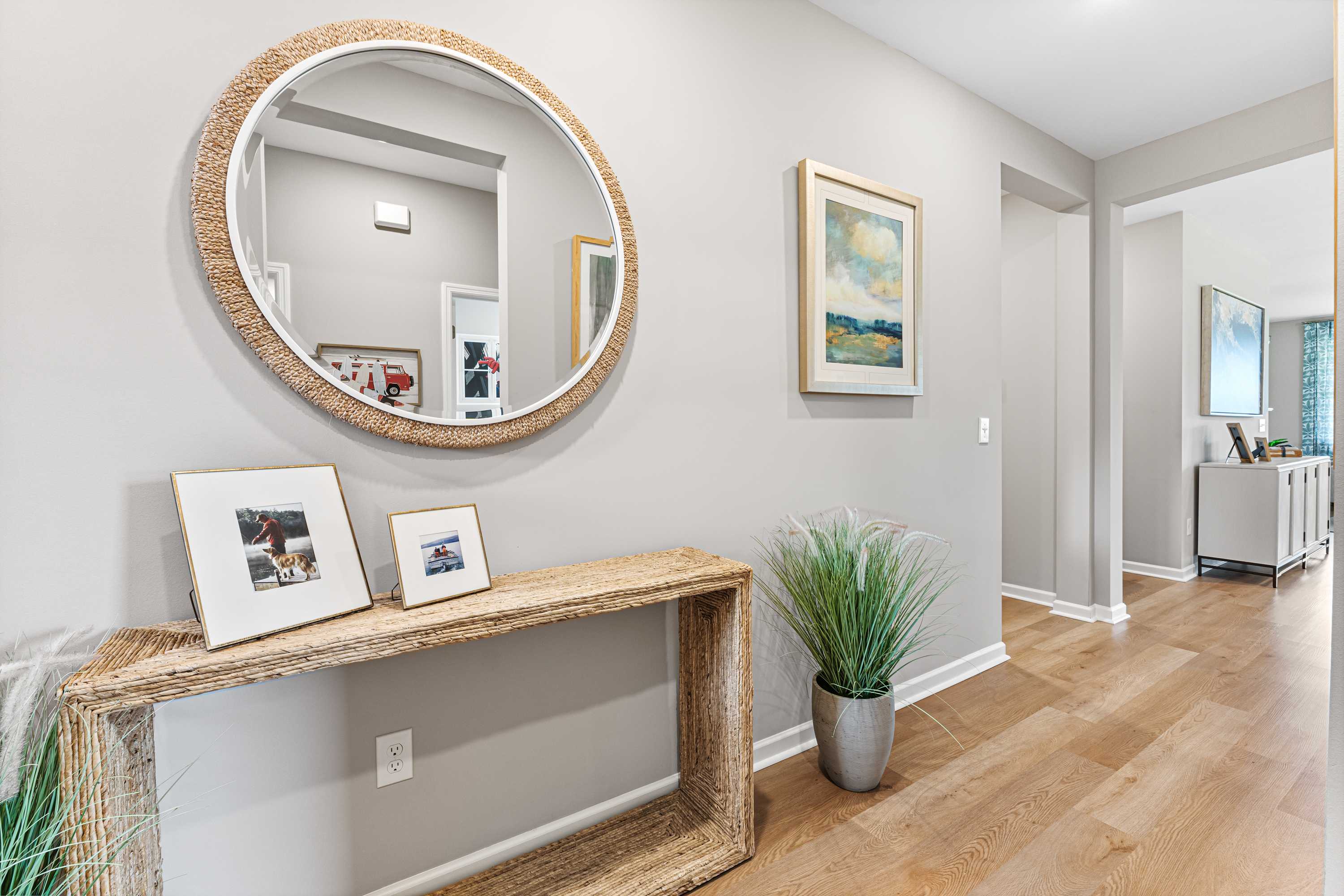 Elegant entryway at Forest Glen in Hazel Green AL featuring rattan mirror, woven console table, potted plant, and hardwood floors