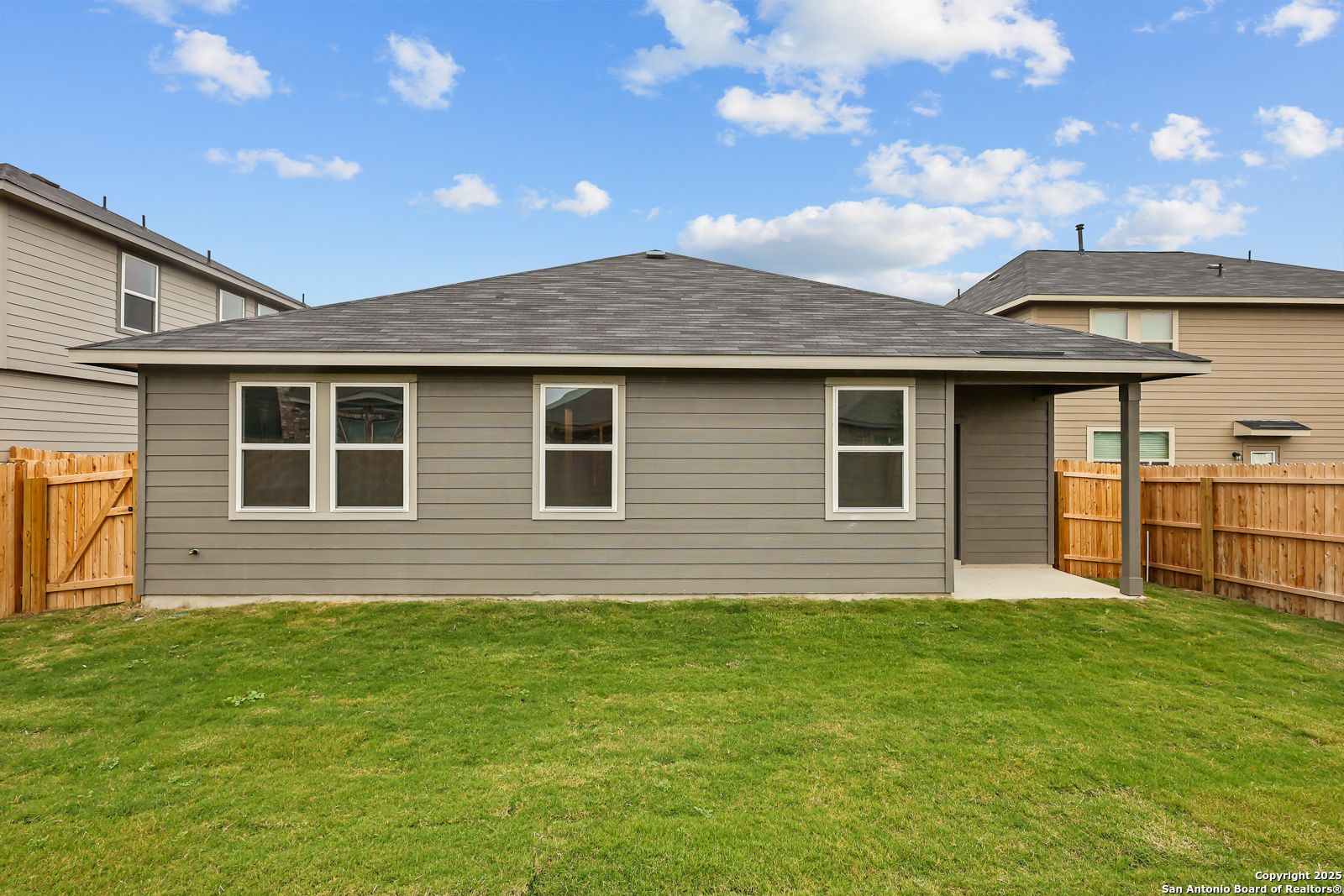 Back view of gray-sided The Daphne J 4-bedroom home featuring covered patio, fenced backyard, and green lawn in Horizon Pointe, Converse, Texas