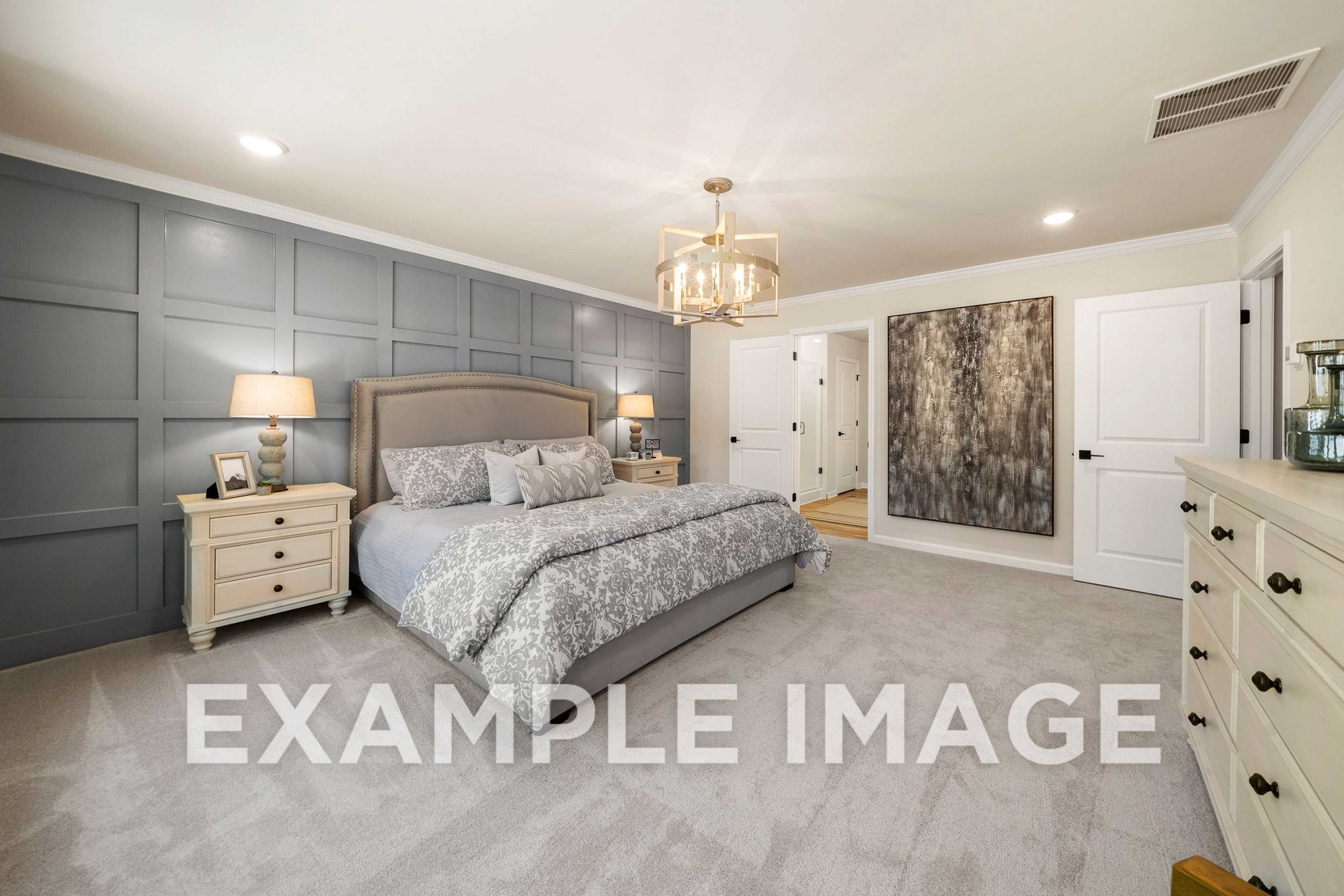 Spacious master bedroom in The Hickory A featuring gray paneled accent wall, king bed with gray bedding, chandelier, and dresser
