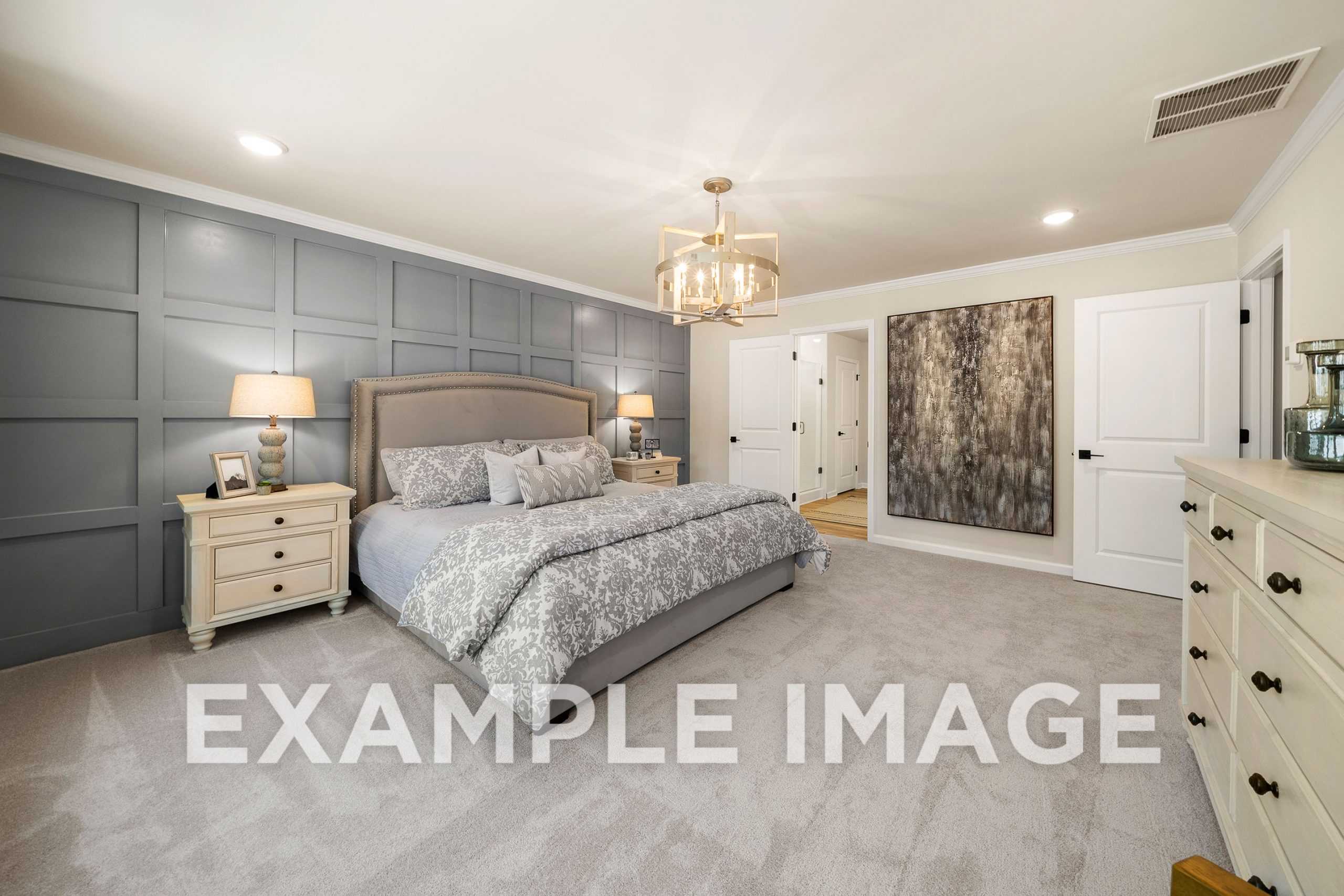 Spacious master bedroom in The Hickory A featuring gray paneled accent wall, king bed with gray bedding, chandelier, and dresser