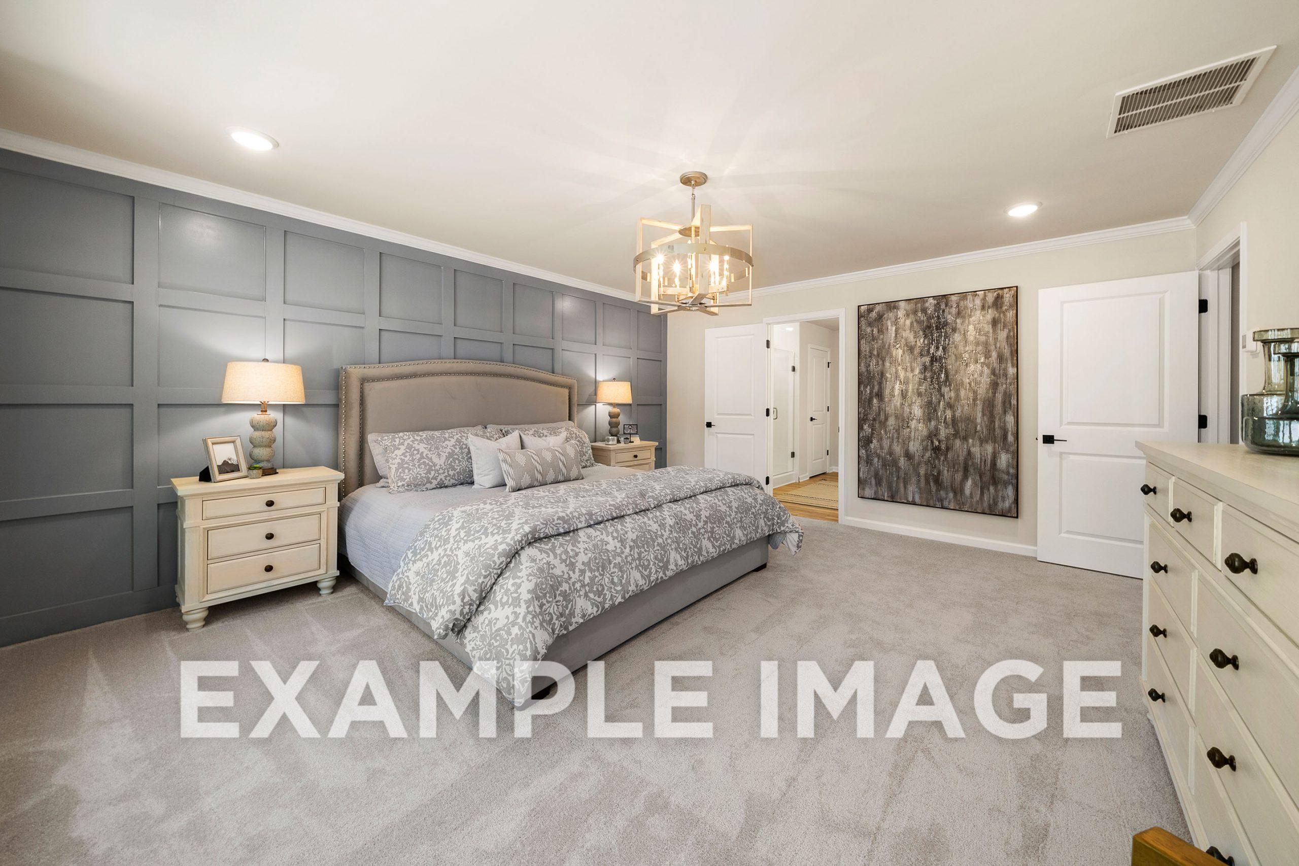 Spacious master bedroom in The Hickory B with gray paneled accent wall, king bed, chandelier, and dresser