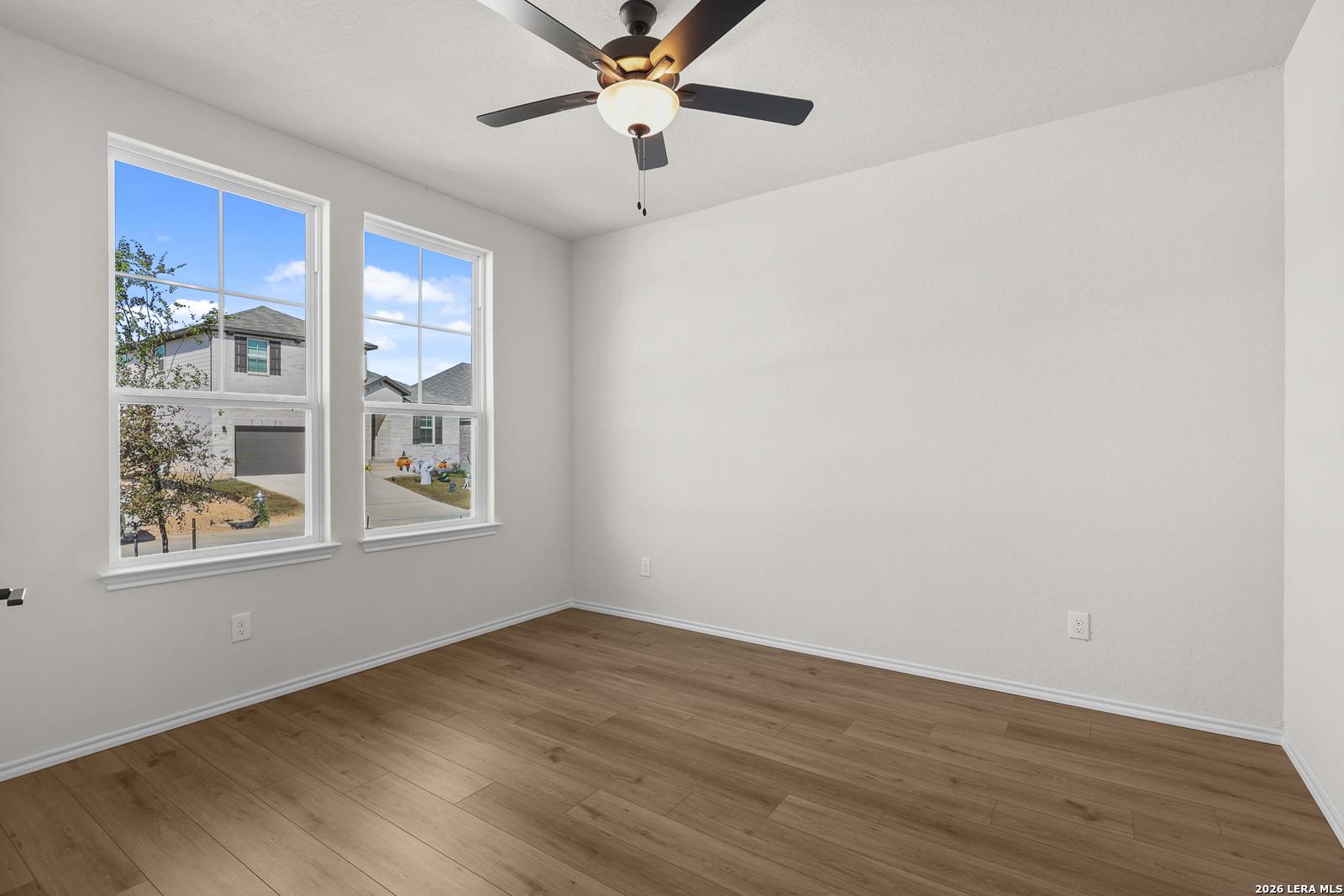 Bright empty bedroom with wood-look flooring, ceiling fan, and double windows in Davidson Homes Glenwood E, Comanche Ridge, San Antonio