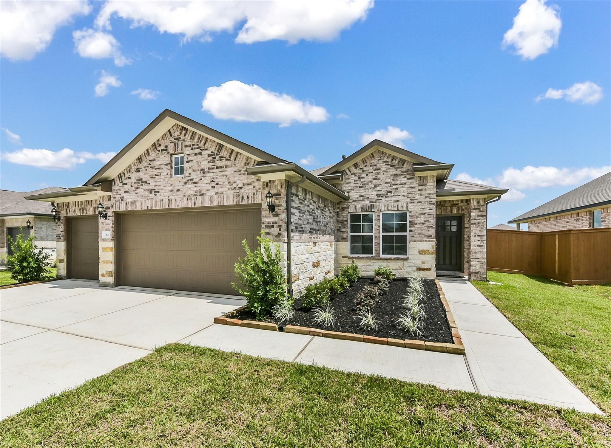 Modern tan brick single-story home with 3-car garage, landscaped yard, and driveway in River Ranch Meadows, Dayton, Texas