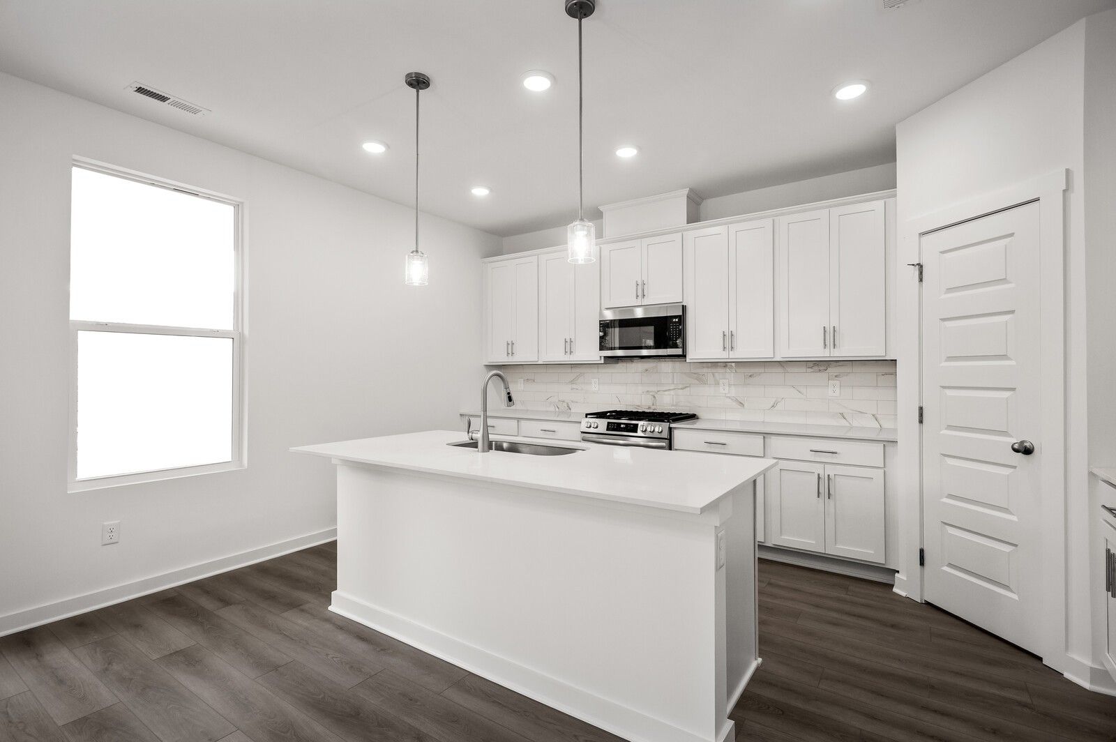 Modern kitchen with white cabinets, quartz island, and stainless appliances in The Logan C floor plan, Calista Farms, TN.