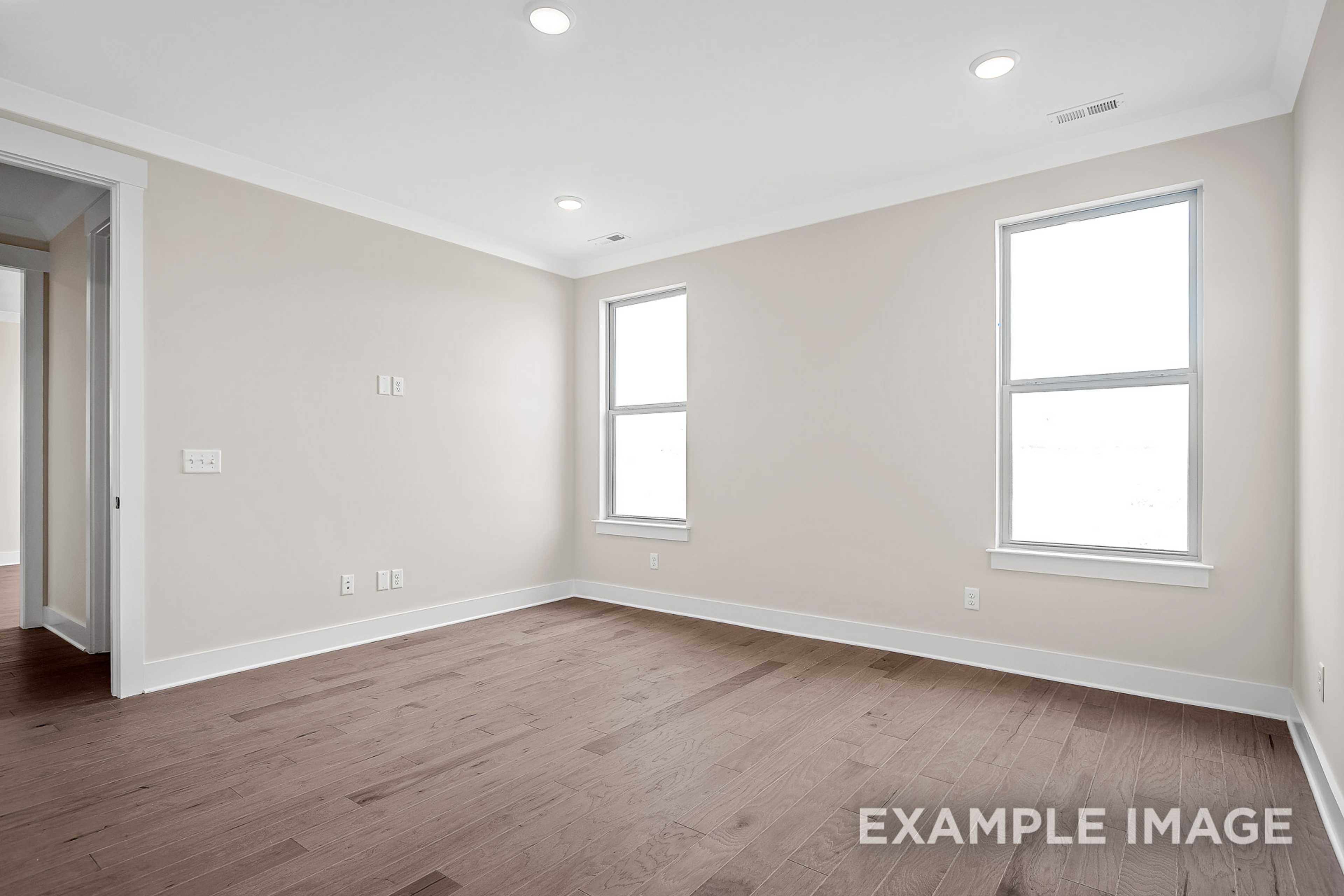 Spacious master bedroom in The Hawkins with beige walls, hardwood floors, recessed lights, and large windows