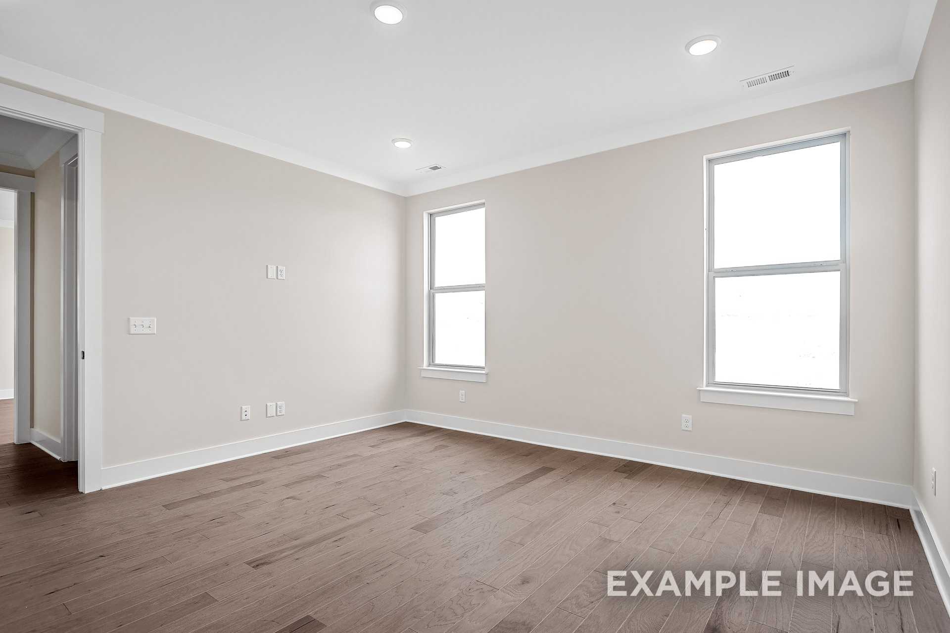 Spacious master bedroom in The Hawkins with beige walls, hardwood floors, recessed lights, and large windows