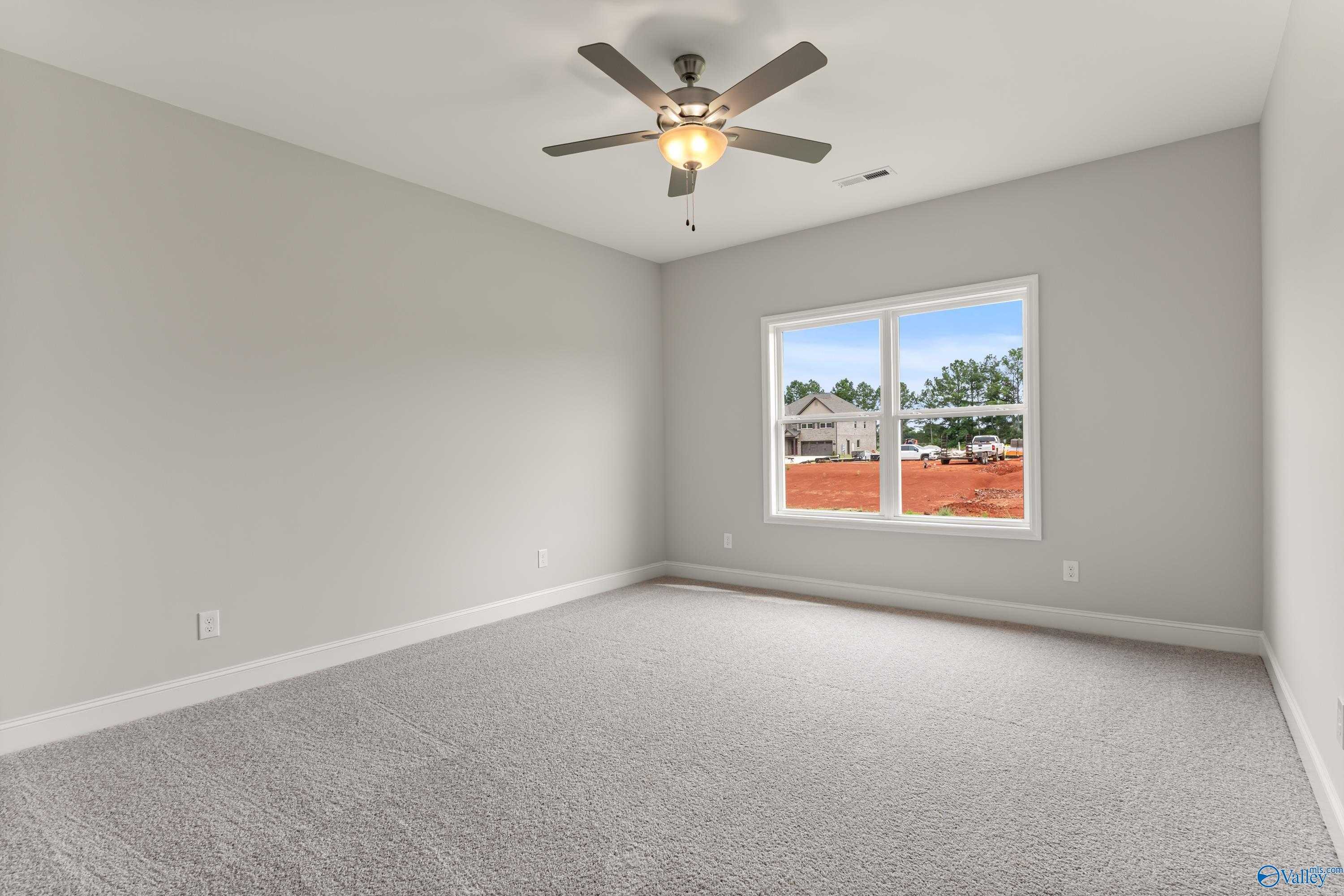 Empty secondary bedroom featuring gray walls, ceiling fan, and window overlooking construction in The Daphne C home, Athens, Alabama