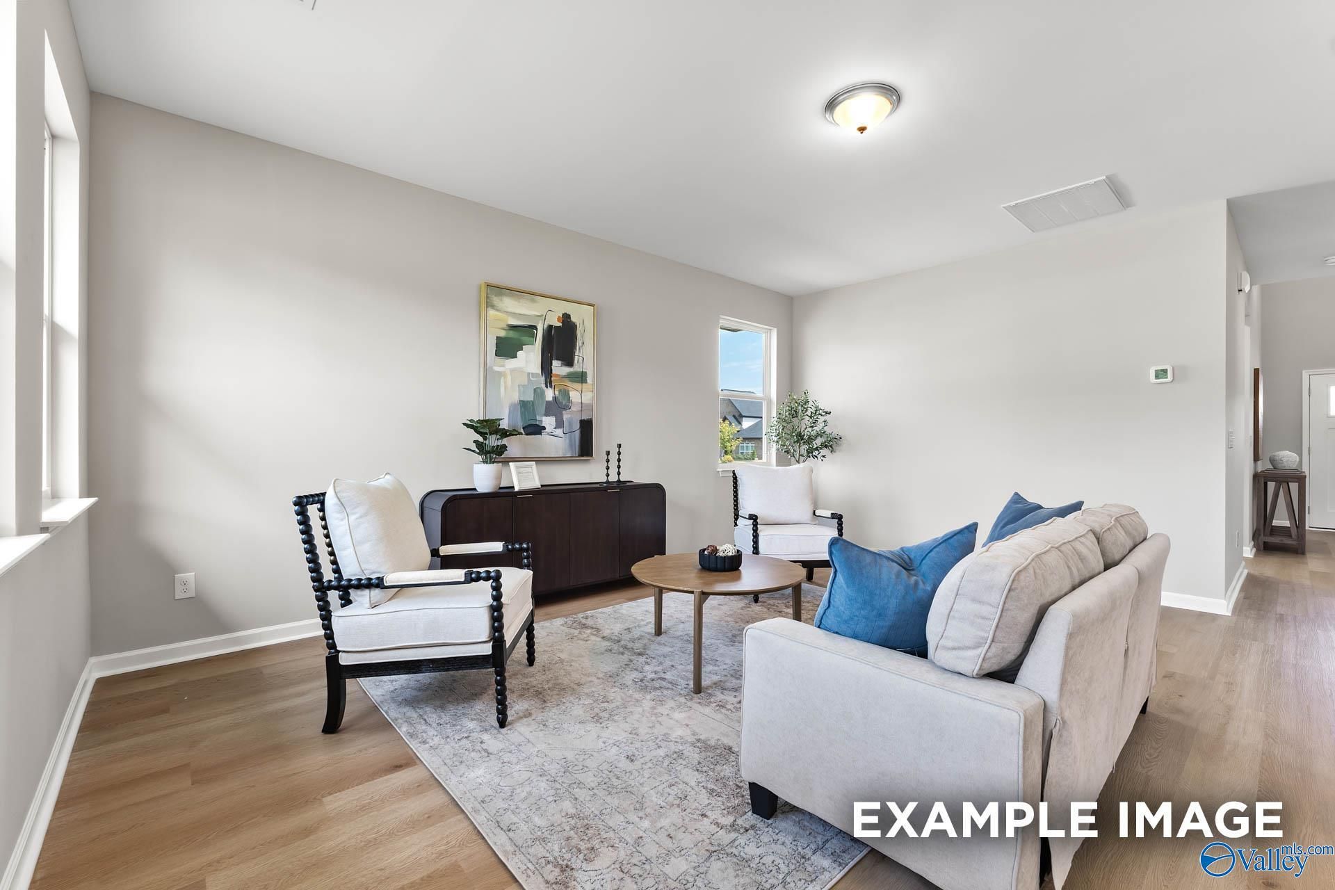 Modern living room with beige sofa, armchairs, abstract art, plants, and hardwood floors in Davidson Homes The Charm, Huntsville