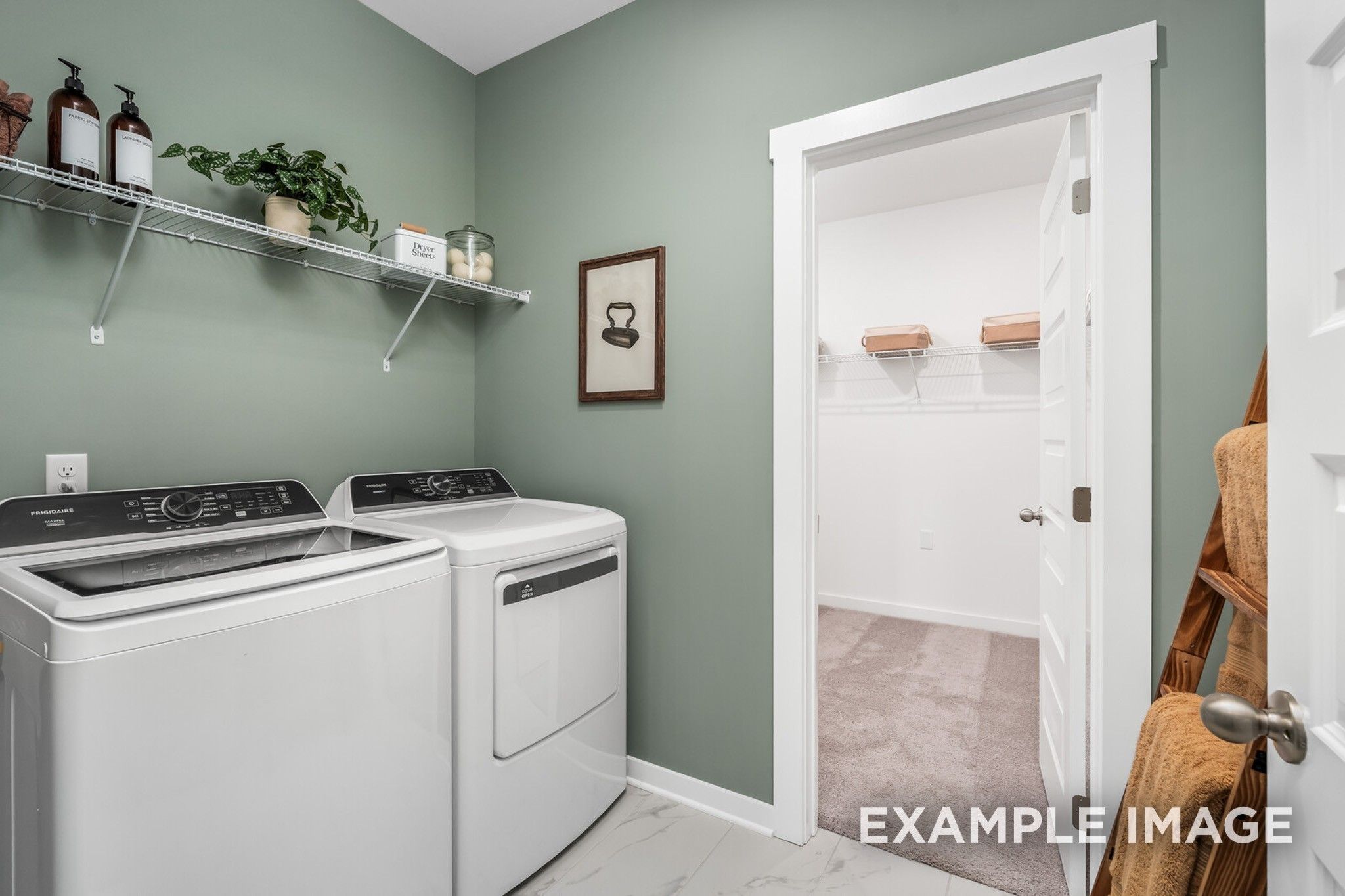 Laundry room with sage green walls, shelving, and attached walk-in storage in The Ash A home at Woods Crossing, Gallatin.