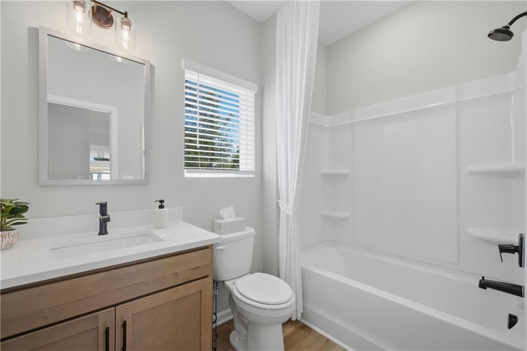 Bright bathroom with wood vanity, white quartz countertop, and tub shower in Davidson Homes Sinclair B, Cartersville, Georgia