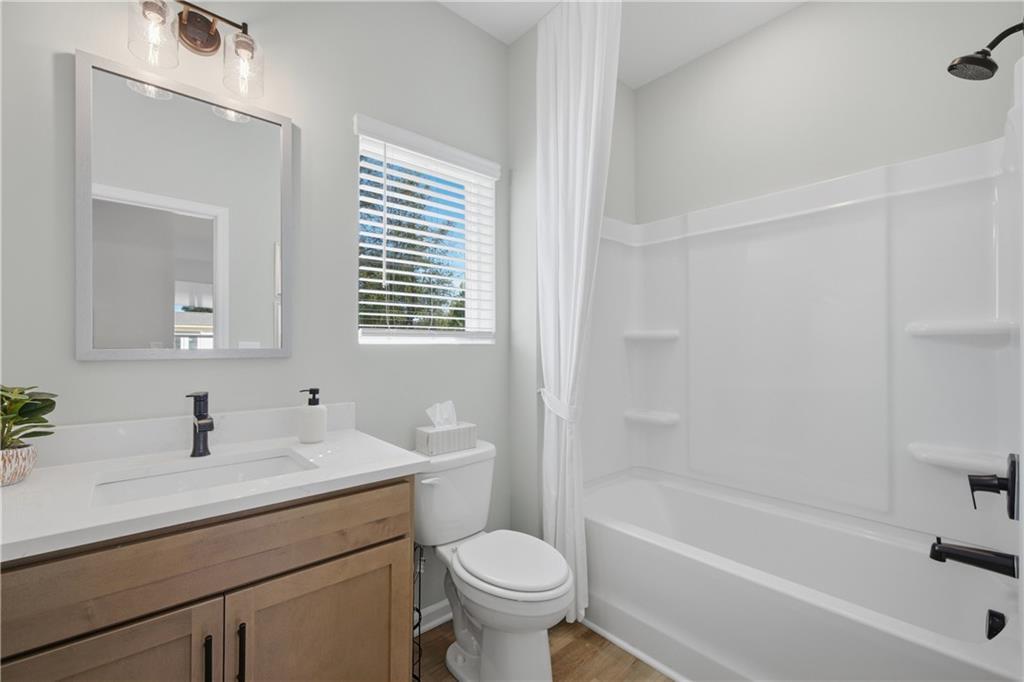 Bright bathroom with wood vanity, white quartz countertop, and tub shower in Davidson Homes Sinclair B, Cartersville, Georgia