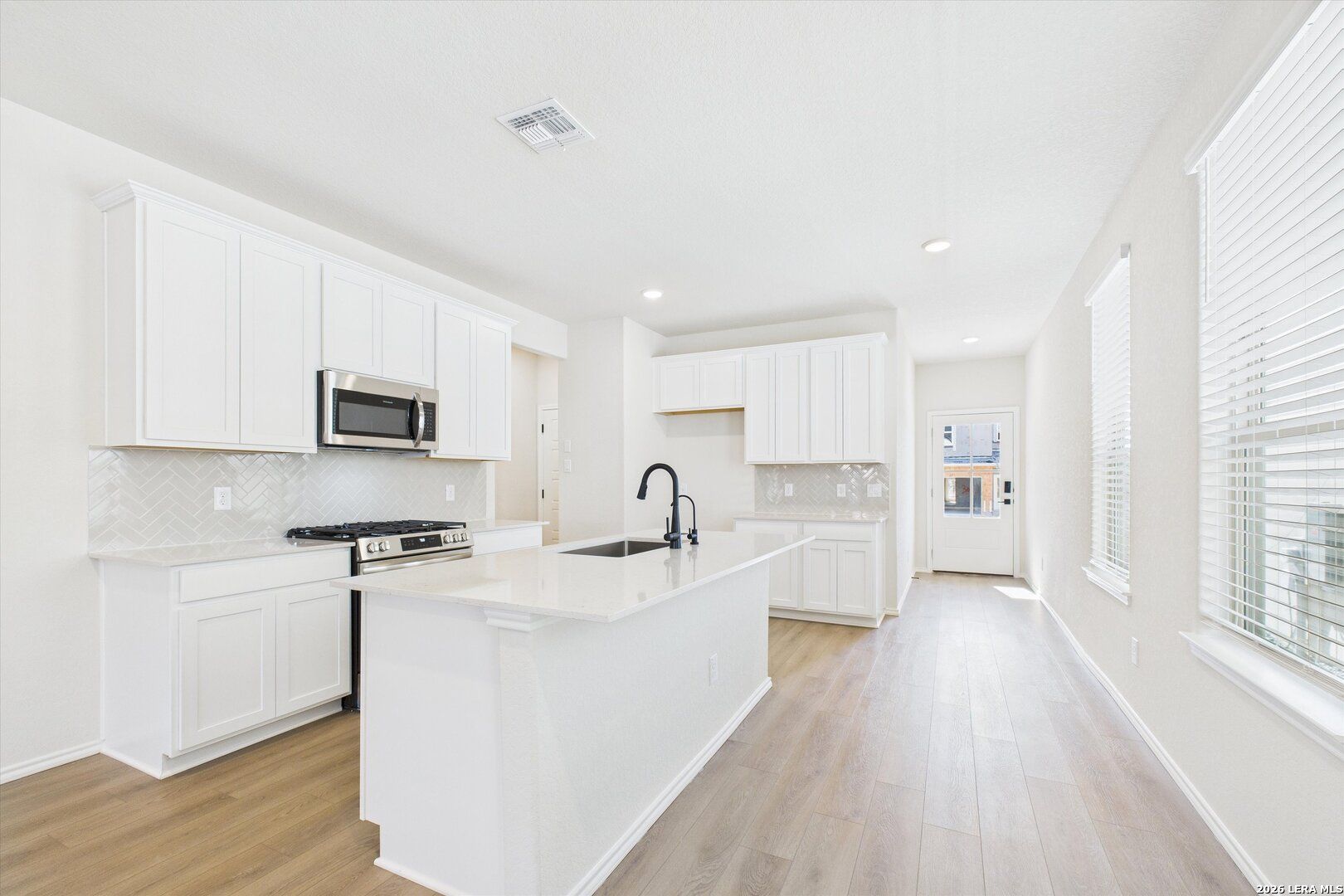 Modern white kitchen with central island, stainless appliances, gas range in The Gillian B by Davidson Homes, San Antonio, Texas