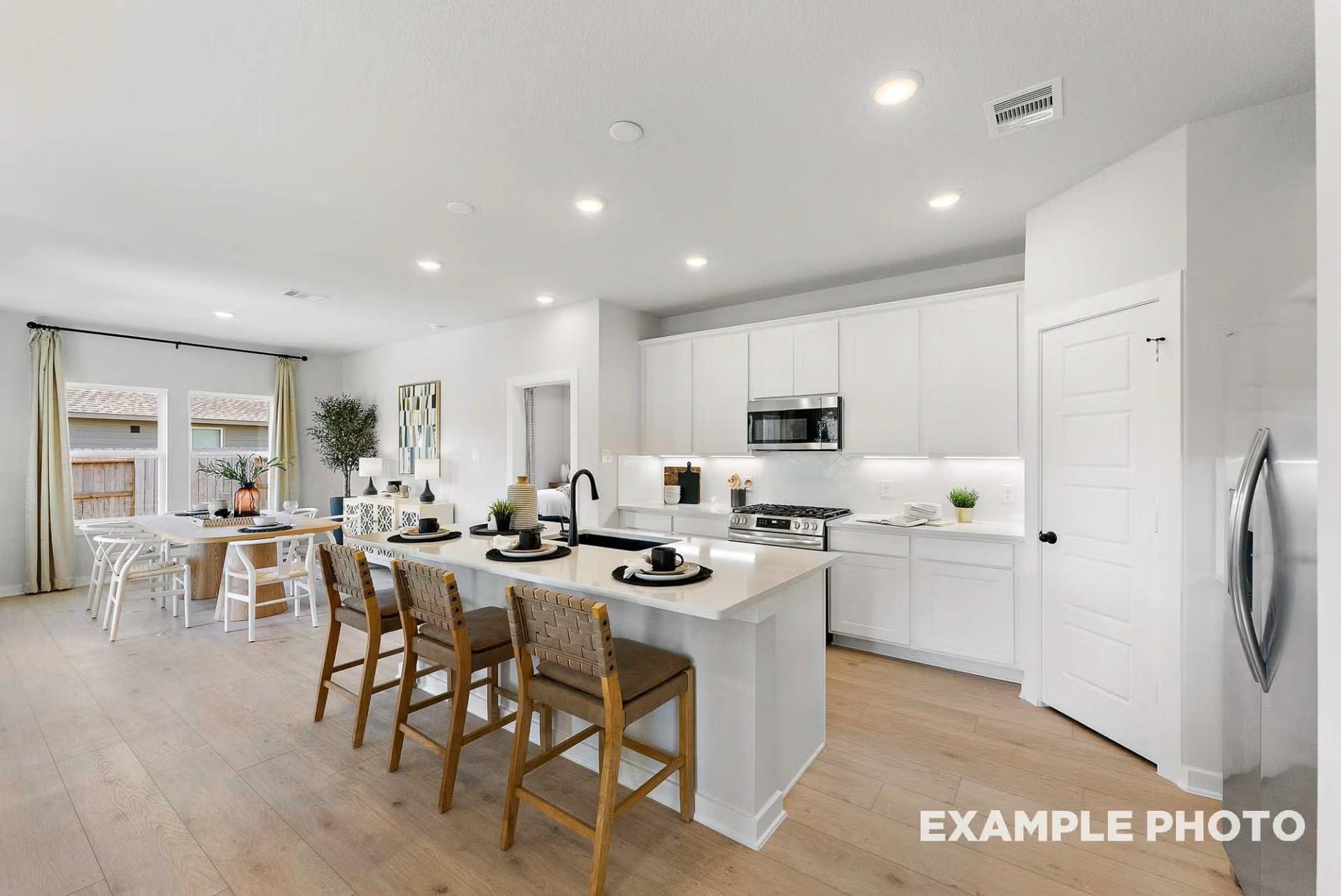 Open-concept white kitchen with quartz island, stainless appliances, and dining nook in Davidson Homes Everett C, Dayton TX