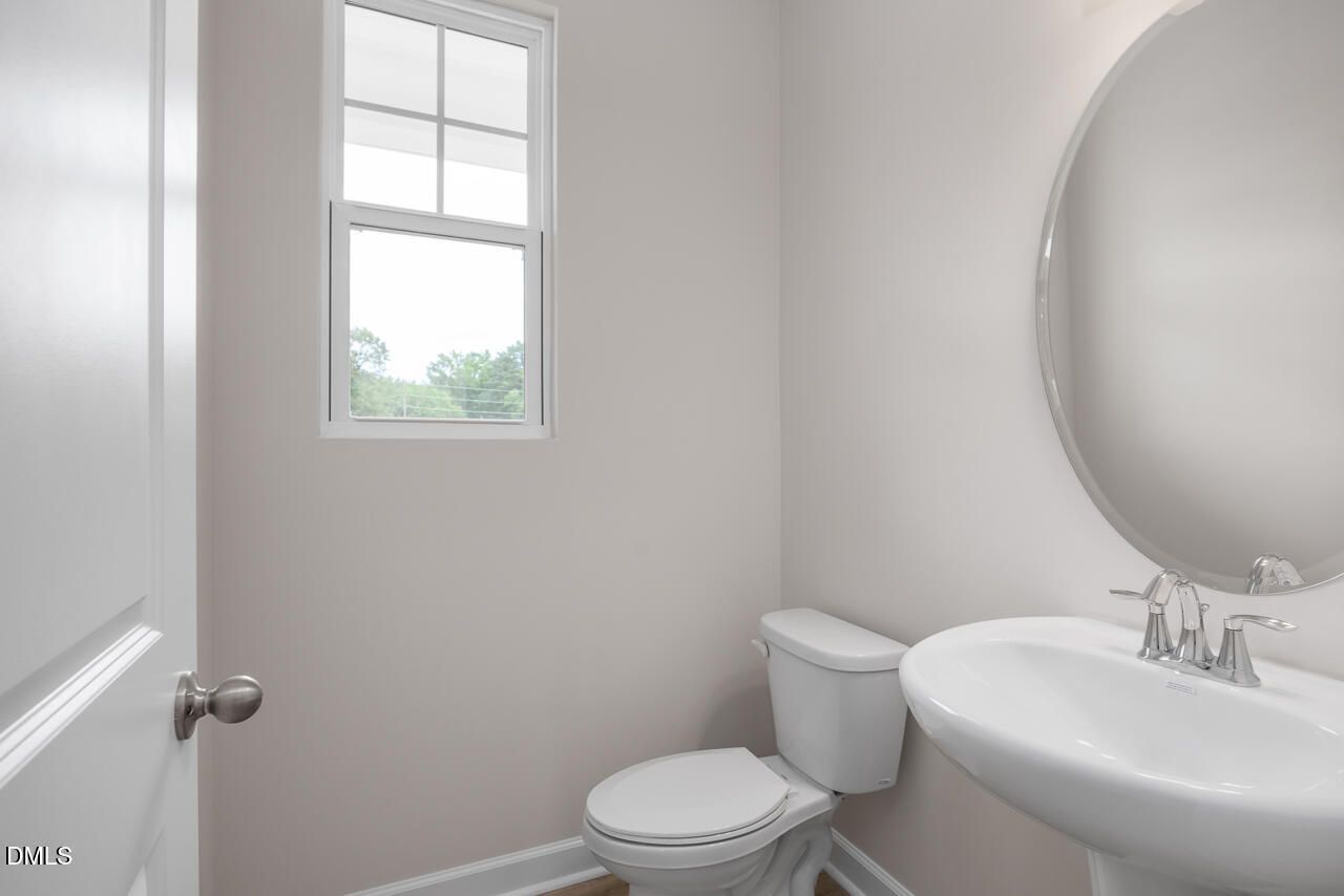 Half bath with pedestal sink, round mirror, and window in The Graham floor plan by Davidson Homes in Springvale, Fuquay-Varina.