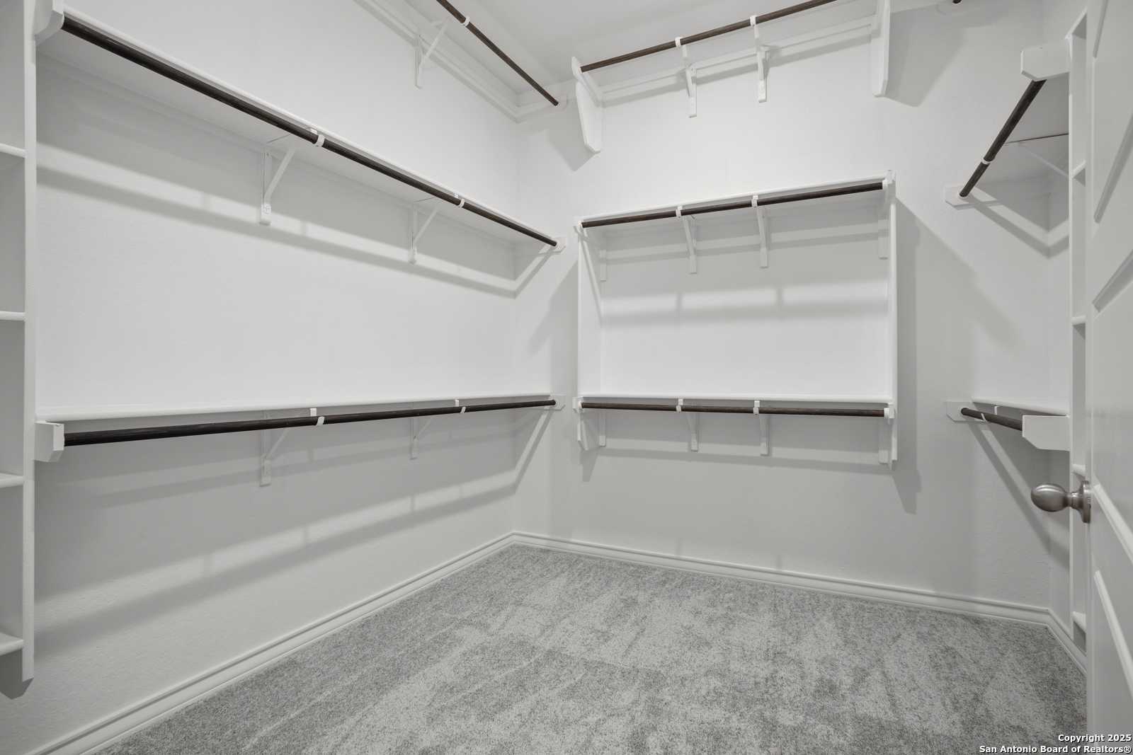Spacious walk-in closet with wooden shelves, hanging rods, white walls, and gray carpet in Davidson Homes The Summerlin B, Castroville, Texas