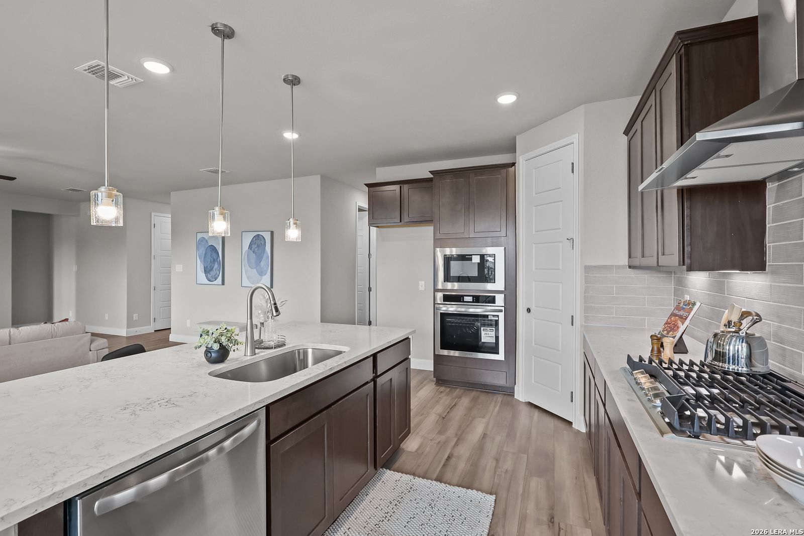 Modern kitchen featuring dark wood cabinets, white quartz island with gas cooktop, stainless double oven in Davidson Homes The Rockford G, San Antonio
