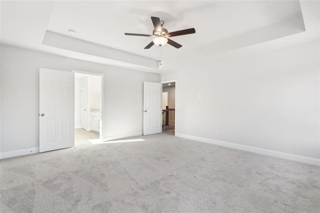 Spacious bedroom with tray ceiling, ceiling fan, and open doors to bathroom in Davidson Homes The Hickory C, Hoschton, GA