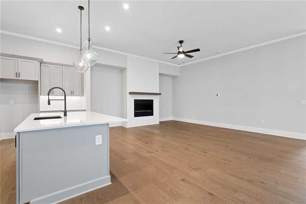 Open-concept kitchen with white island sink, pendant lights, and adjacent great room featuring white brick fireplace, hardwood floors in Davidson Homes The Seaside B, Woodstock, GA