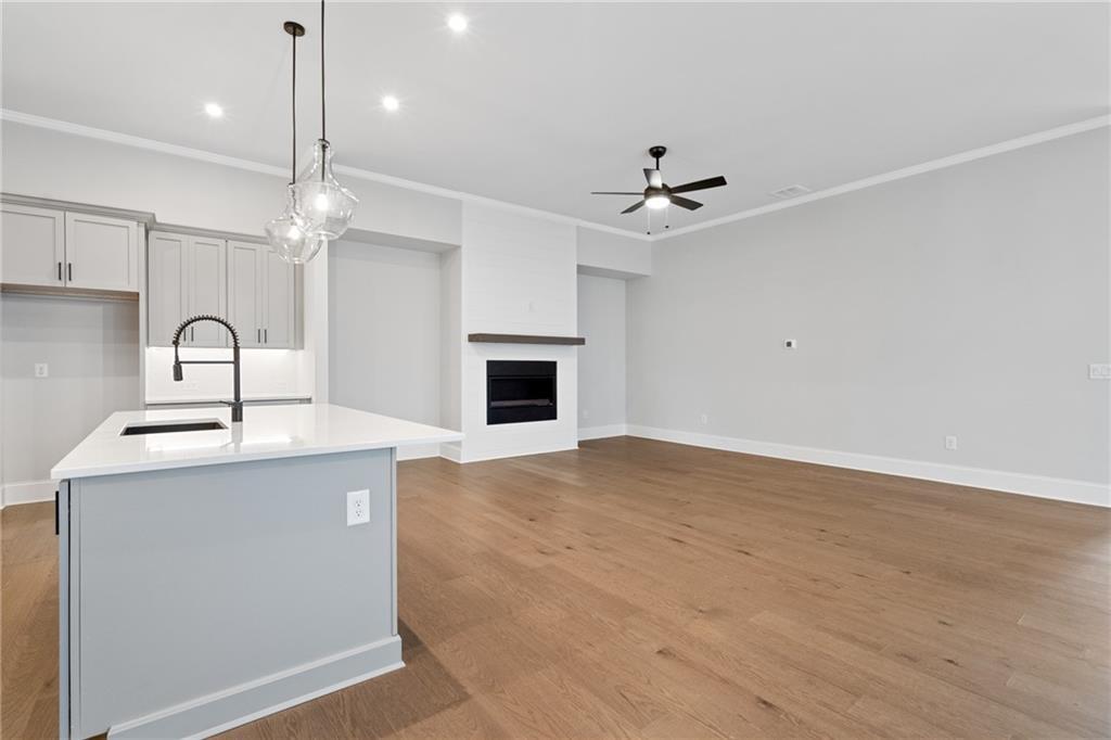 Open-concept kitchen with white island sink, pendant lights, and adjacent great room featuring white brick fireplace, hardwood floors in Davidson Homes The Seaside B, Woodstock, GA