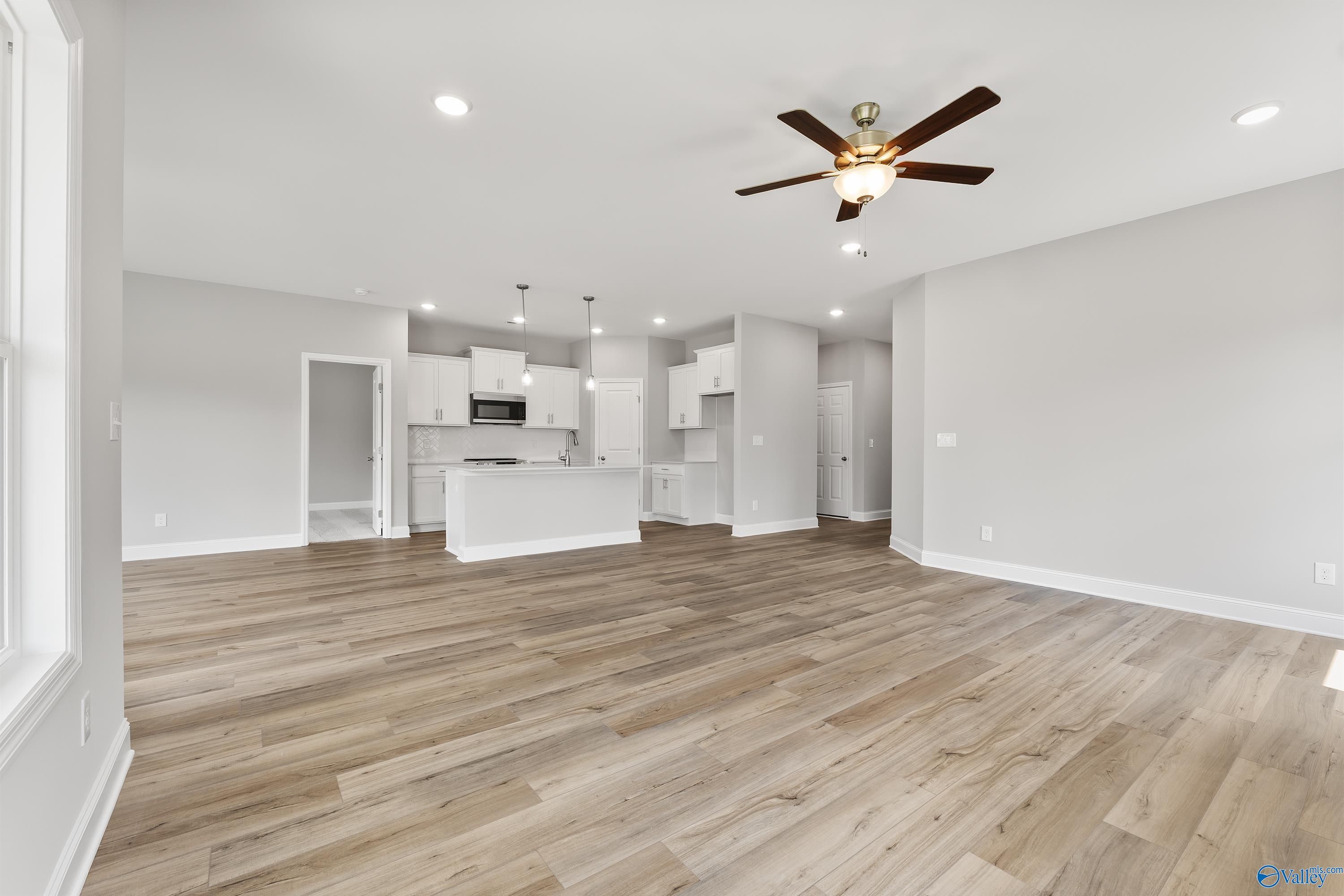 Open-concept kitchen and living area with white cabinets, center island, ceiling fans, and hardwood-look floors in Davidson Homes Franklin C, Huntsville AL