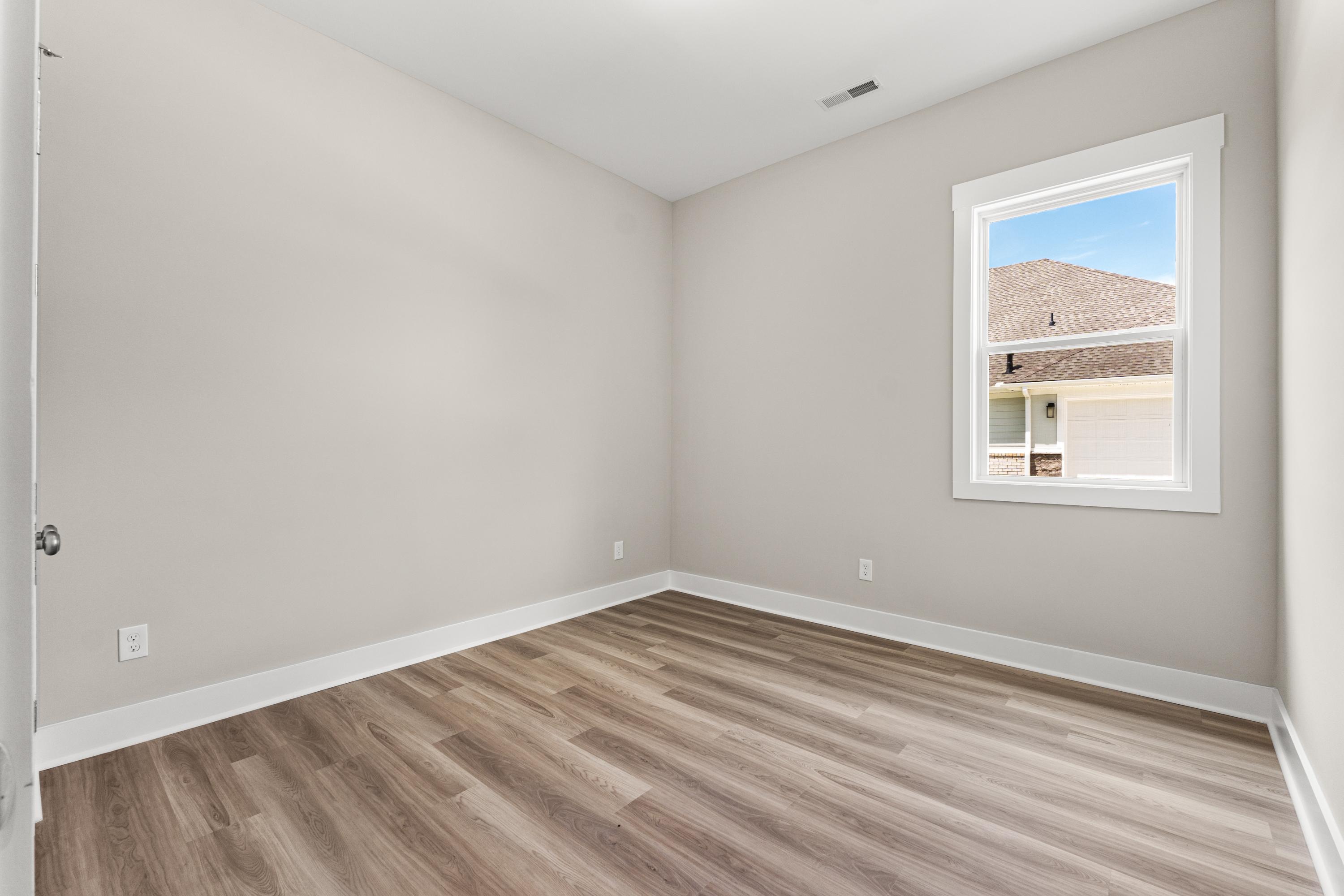 Spacious empty bedroom in The Oxford A home with neutral gray walls, large window, and luxury vinyl plank wood flooring